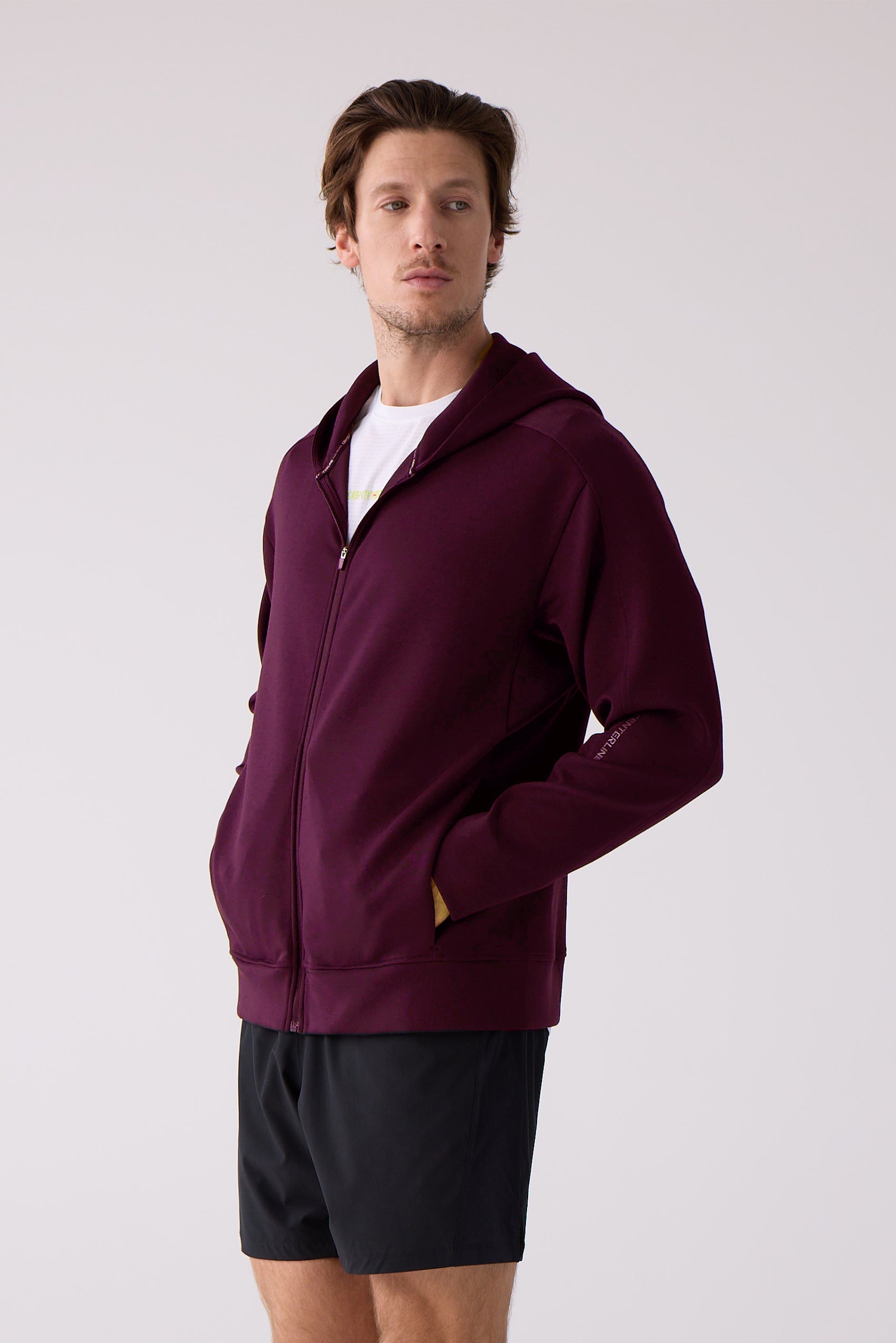 Maroon Après Unisex sweatshirt by Centerline Athletics, featuring a full-zip front, hood, and 'Centerline' text on the sleeve, styled on a model wearing black shorts.