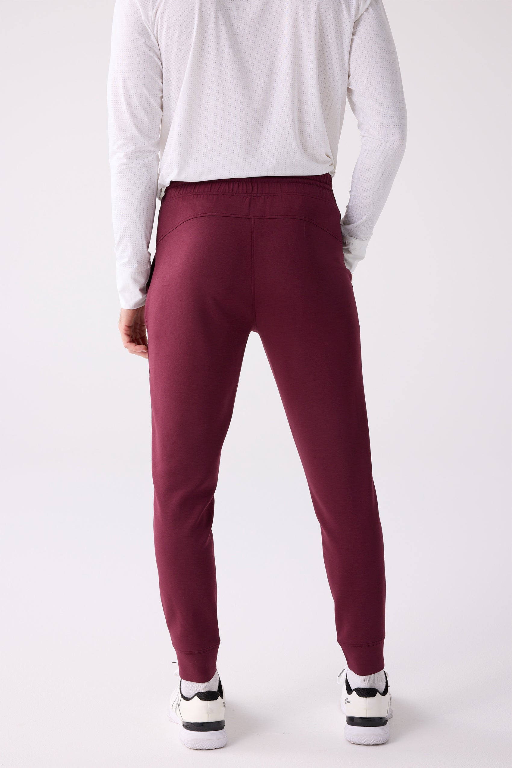 Maroon men's jogger by Centerline Athletics, shown from the back, with an elastic waistband and cuffed ankles, worn with a white long-sleeve shirt and white sneakers.