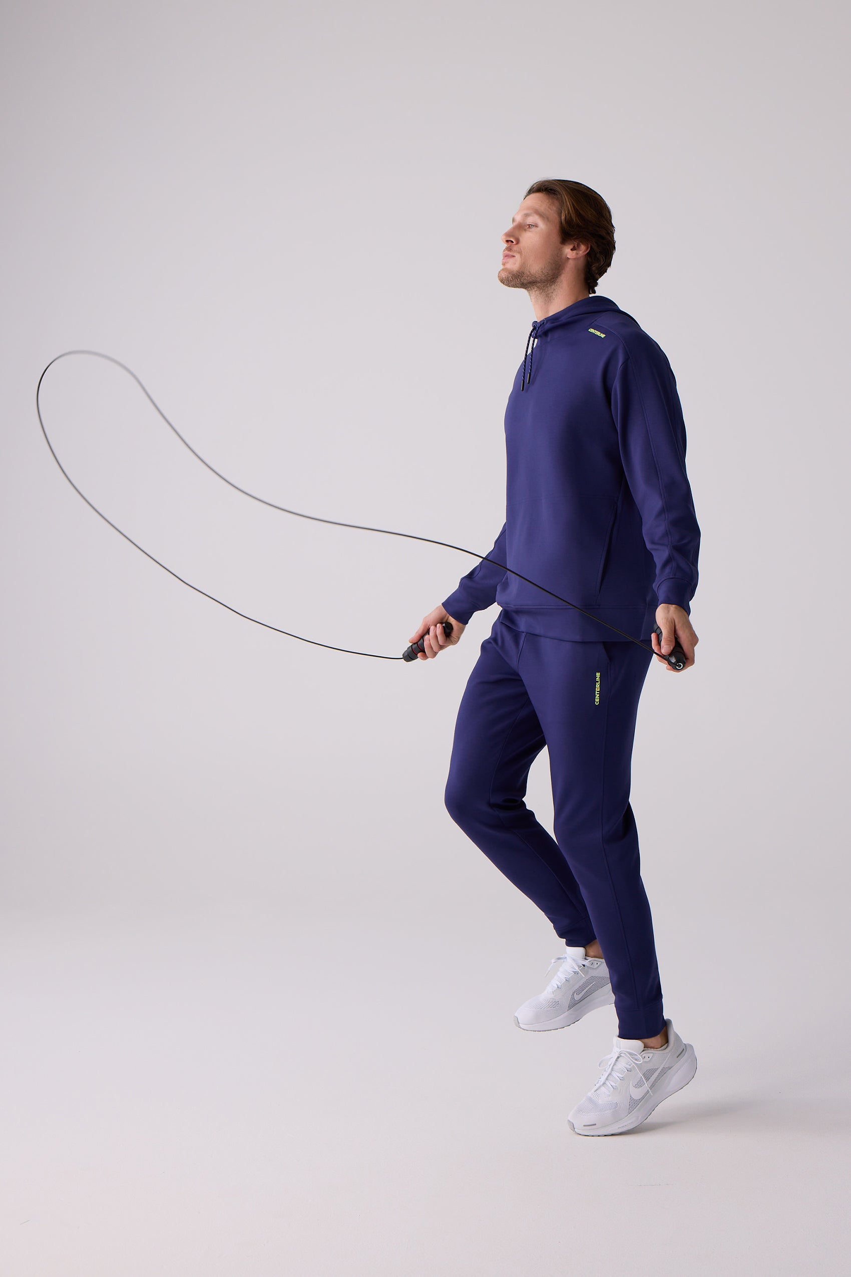 Dark blue Men's Après Jogger by Centerline Athletics, featuring a lime green logo on the left thigh, worn by a man skipping rope.