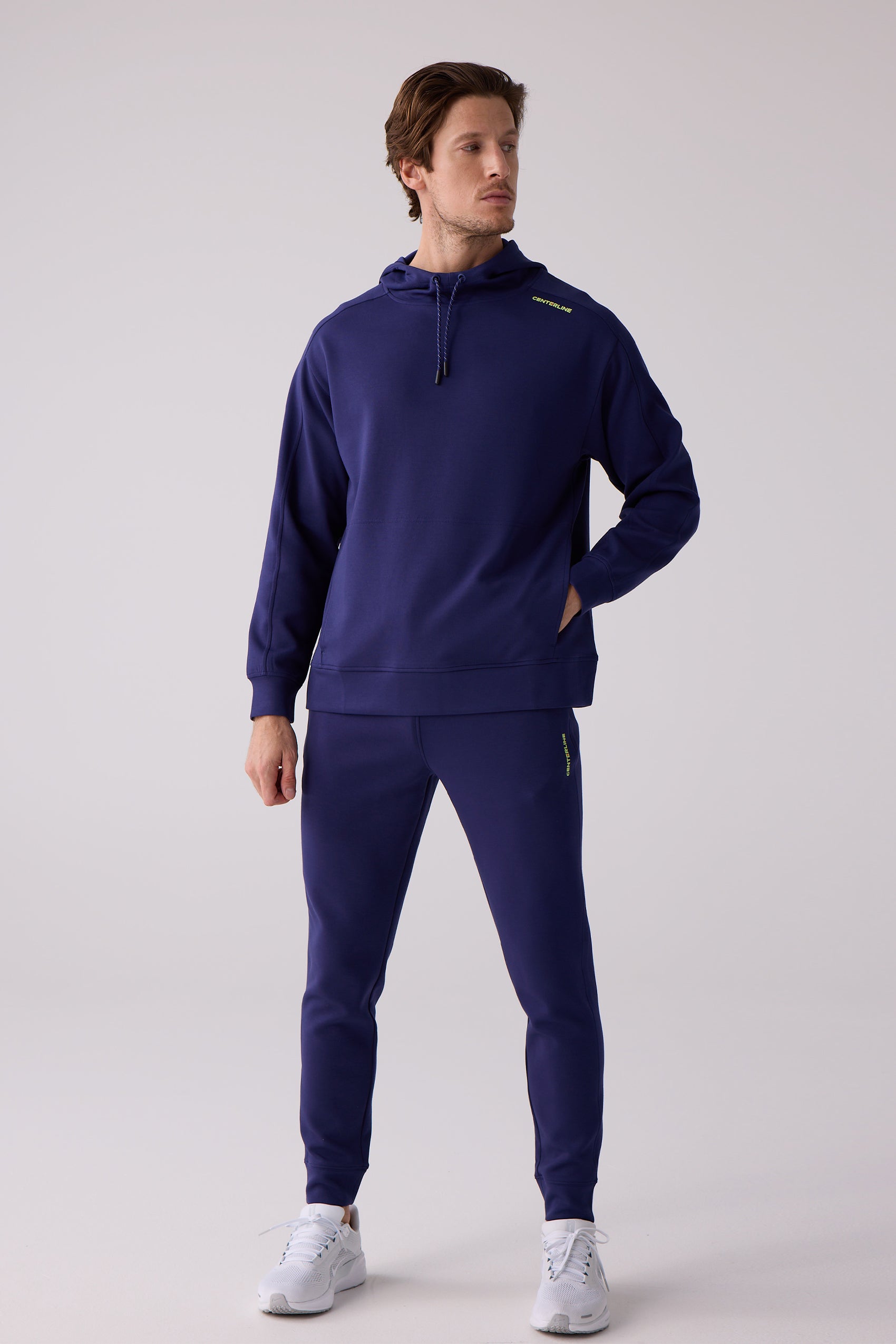 Men's deep navy blue Après Jogger by Centerline Athletics with a yellow-green logo, styled with a matching hoodie and white sneakers.
