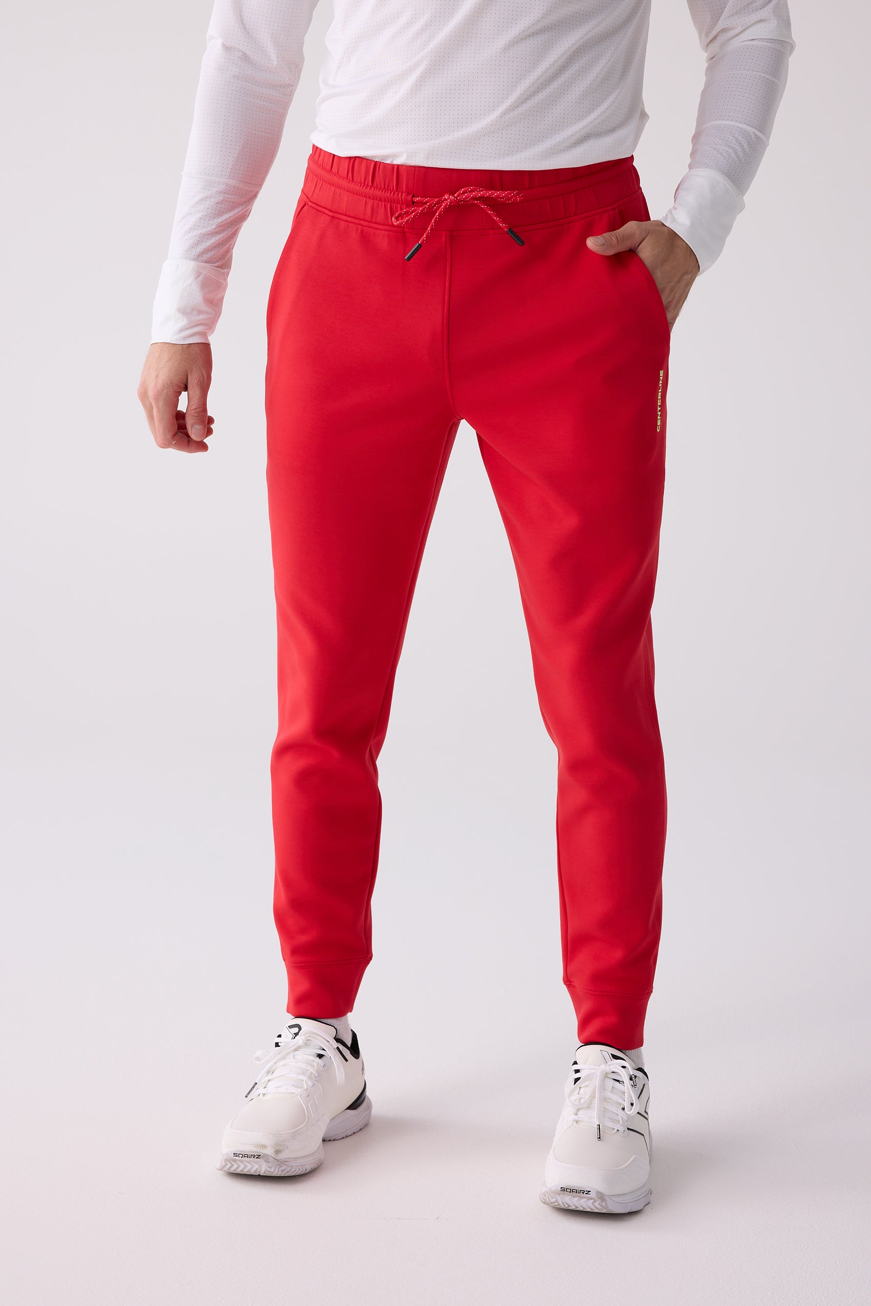 Red Men's Après Jogger by Centerline Athletics, featuring a red drawstring waist, vertical yellow logo, and tapered fit, styled with a white long-sleeve shirt and sneakers.