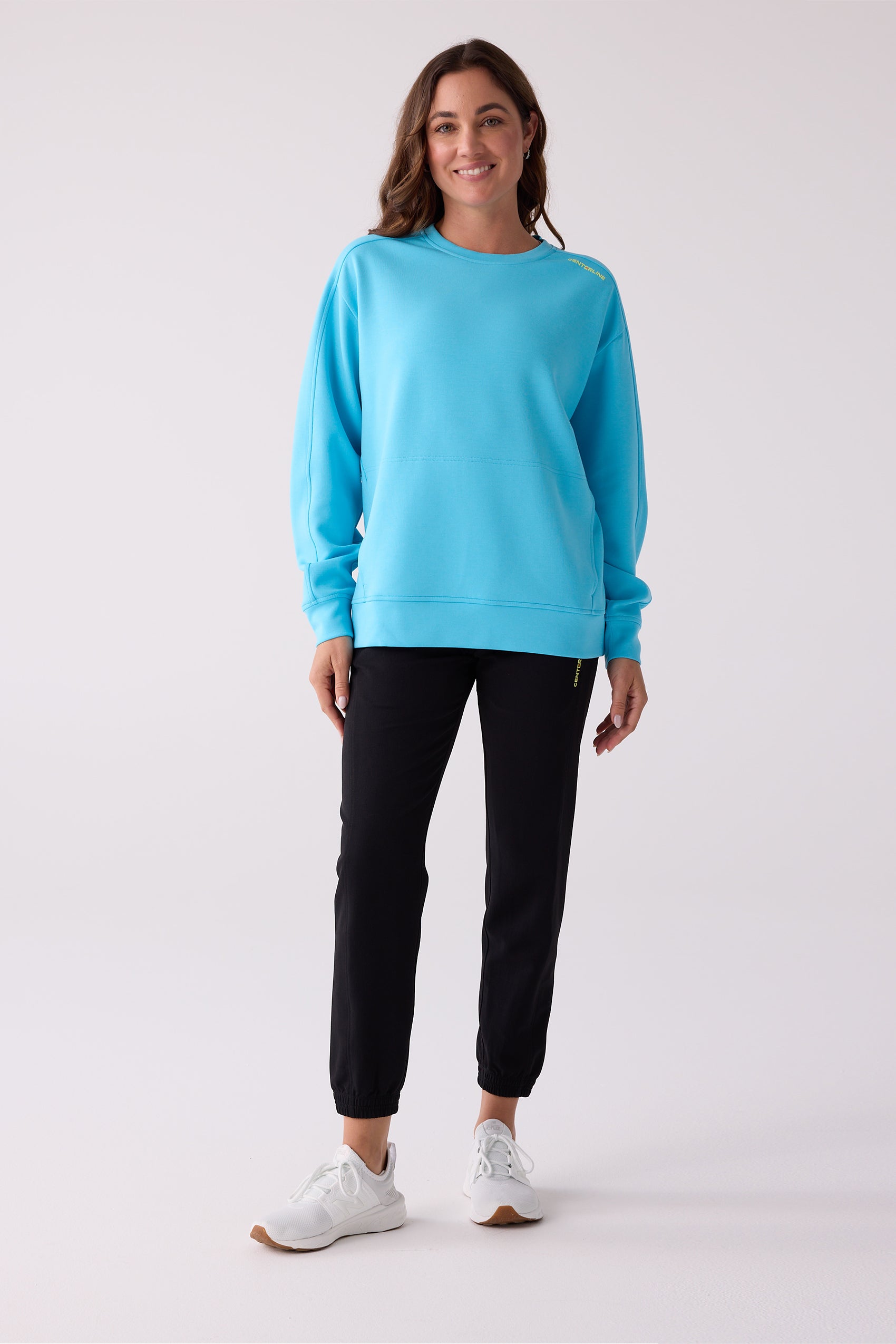 Bright blue Après crew sweatshirt by Centerline Athletics, with a front panel and yellow logo text, styled with black joggers and white sneakers.