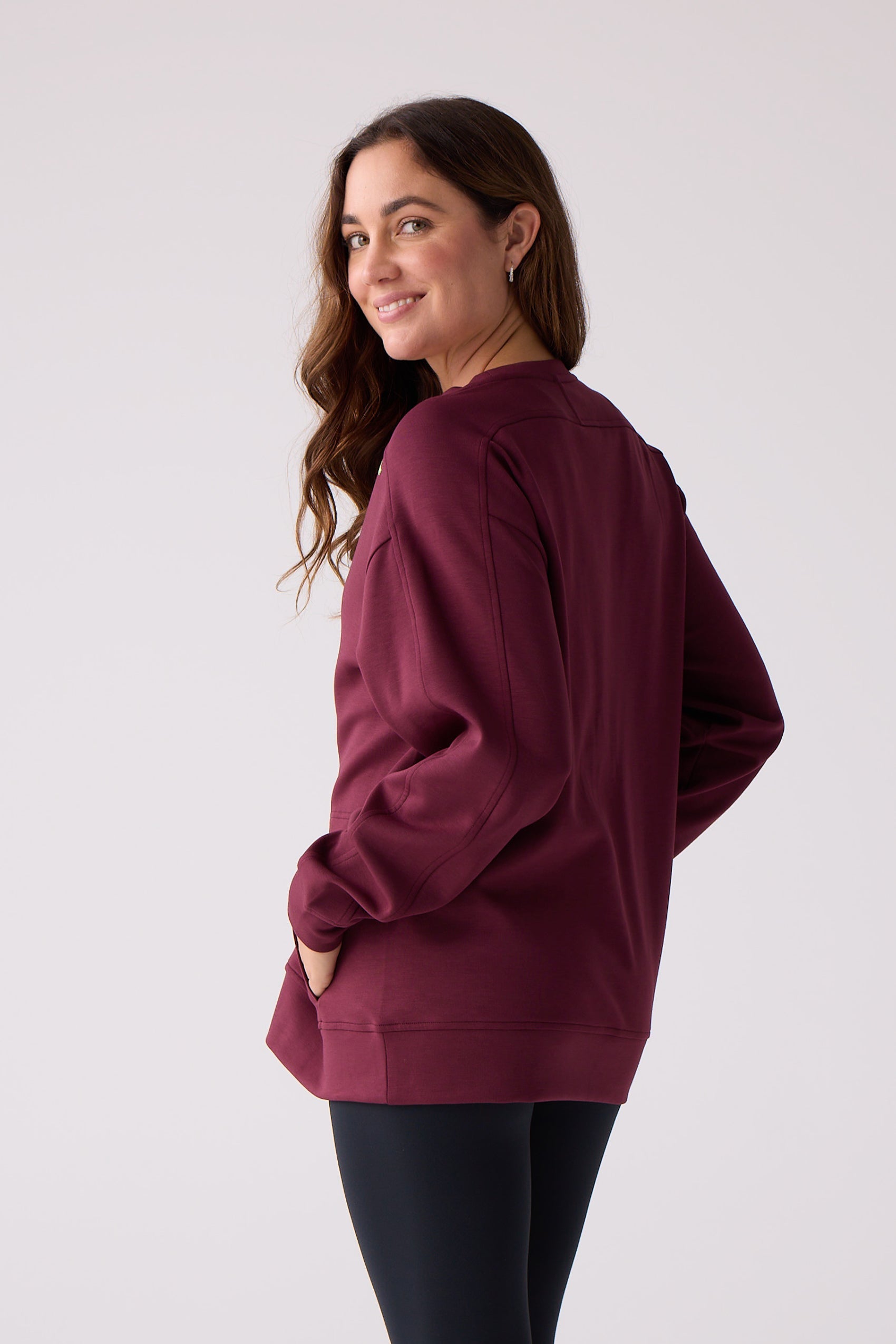 Maroon women's crew sweatshirt by Centerline Athletics, with visible seam details, worn by a smiling model looking over her shoulder over black leggings.