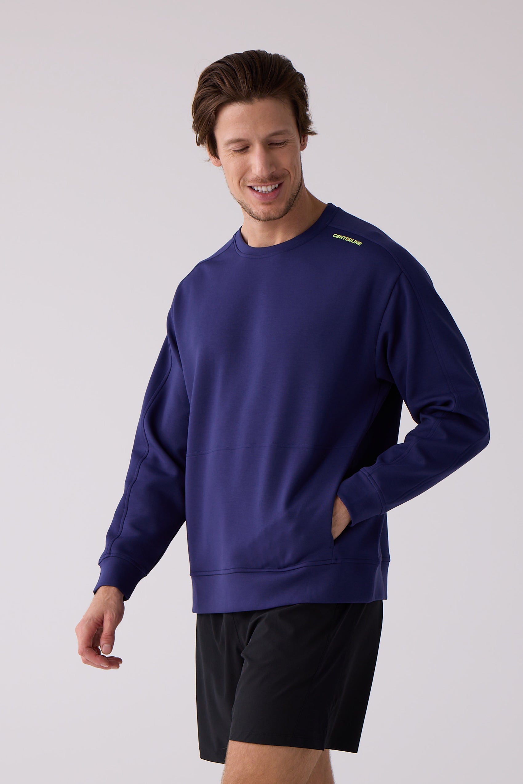 Navy blue men's crew sweatshirt by Centerline Athletics with a lime green shoulder logo and front pouch pocket, worn with black shorts.