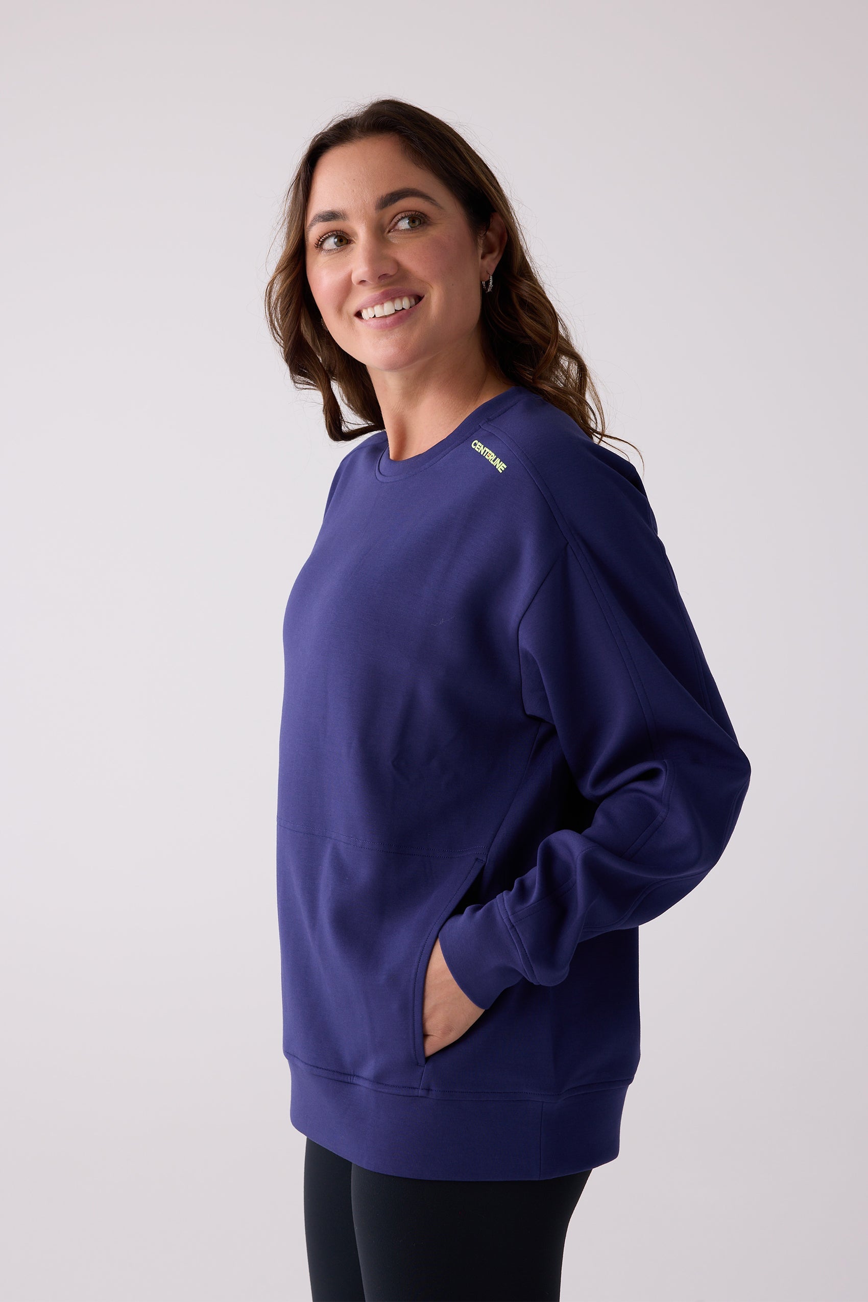 Deep blue crew sweatshirt by Centerline Athletics with front pocket and yellow 'CENTERLINE' logo on the shoulder, styled on a smiling model.