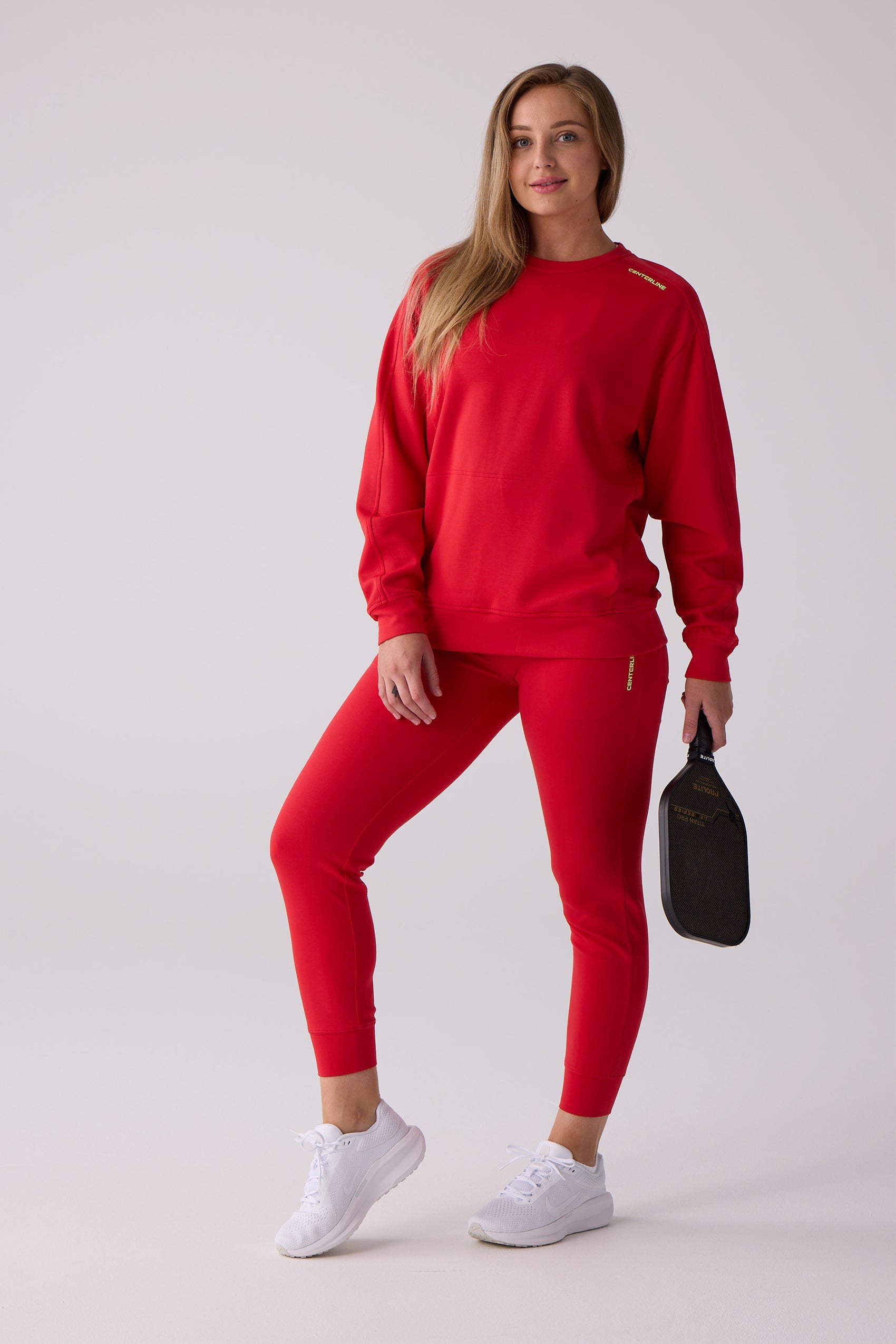 Red crew sweatshirt by Centerline Athletics, styled with matching red leggings and white sneakers, holding a black pickleball paddle.