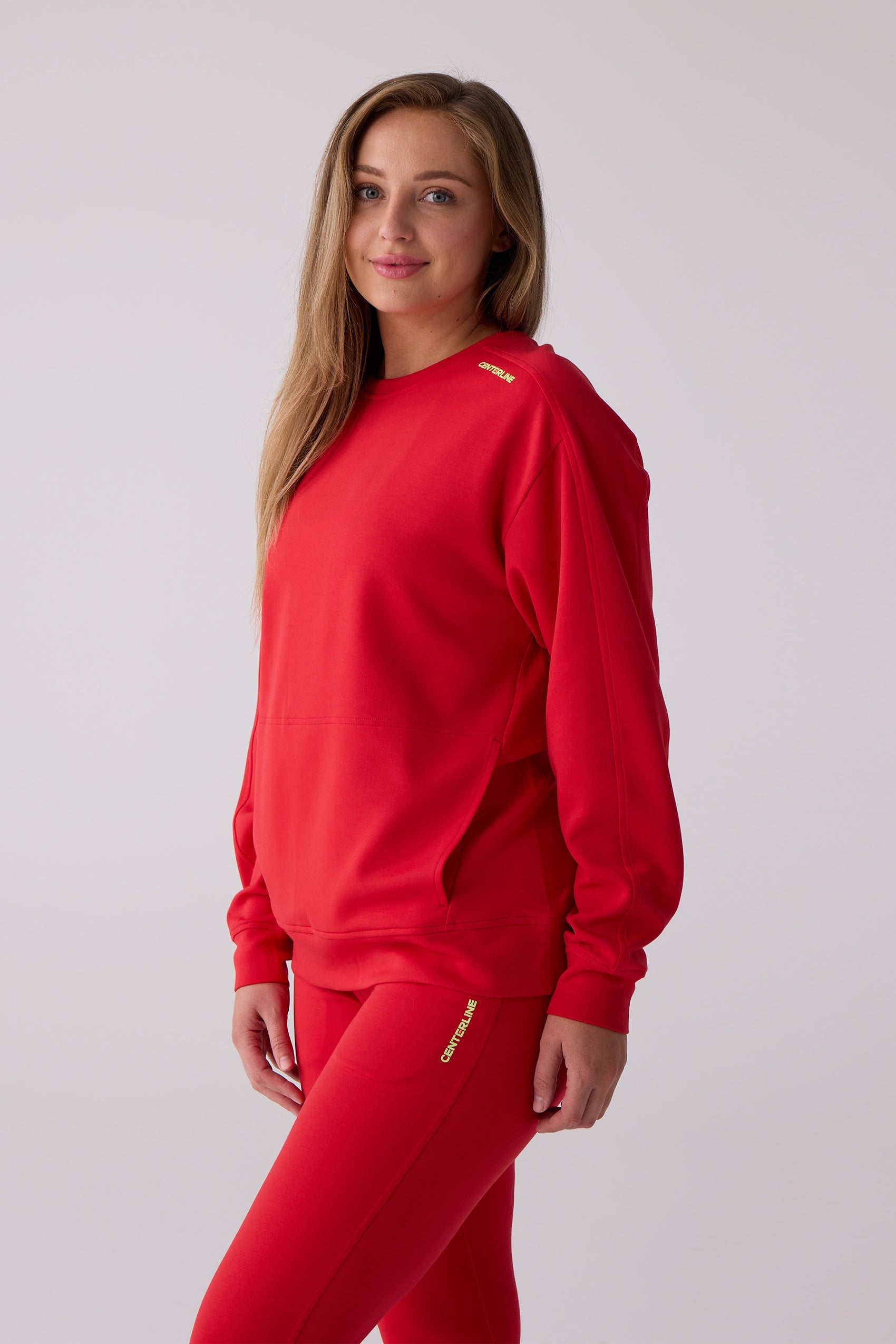 Red Women's Crew Sweatshirt by Centerline Athletics with yellow shoulder logo and front pocket, paired with matching leggings.