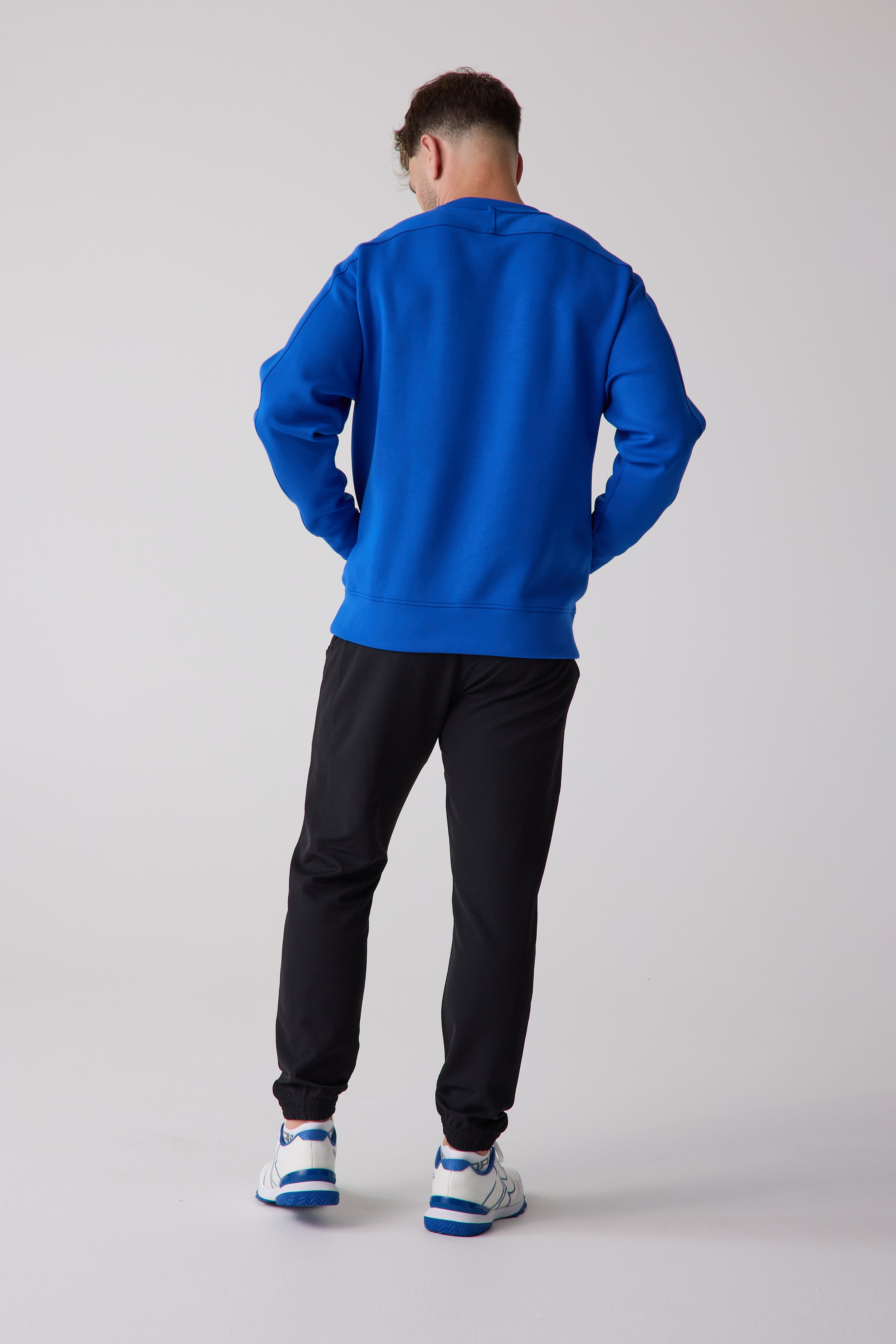 Royal blue men's crew sweatshirt by Centerline Athletics, viewed from the back, with black sweatpants and white and blue sneakers.