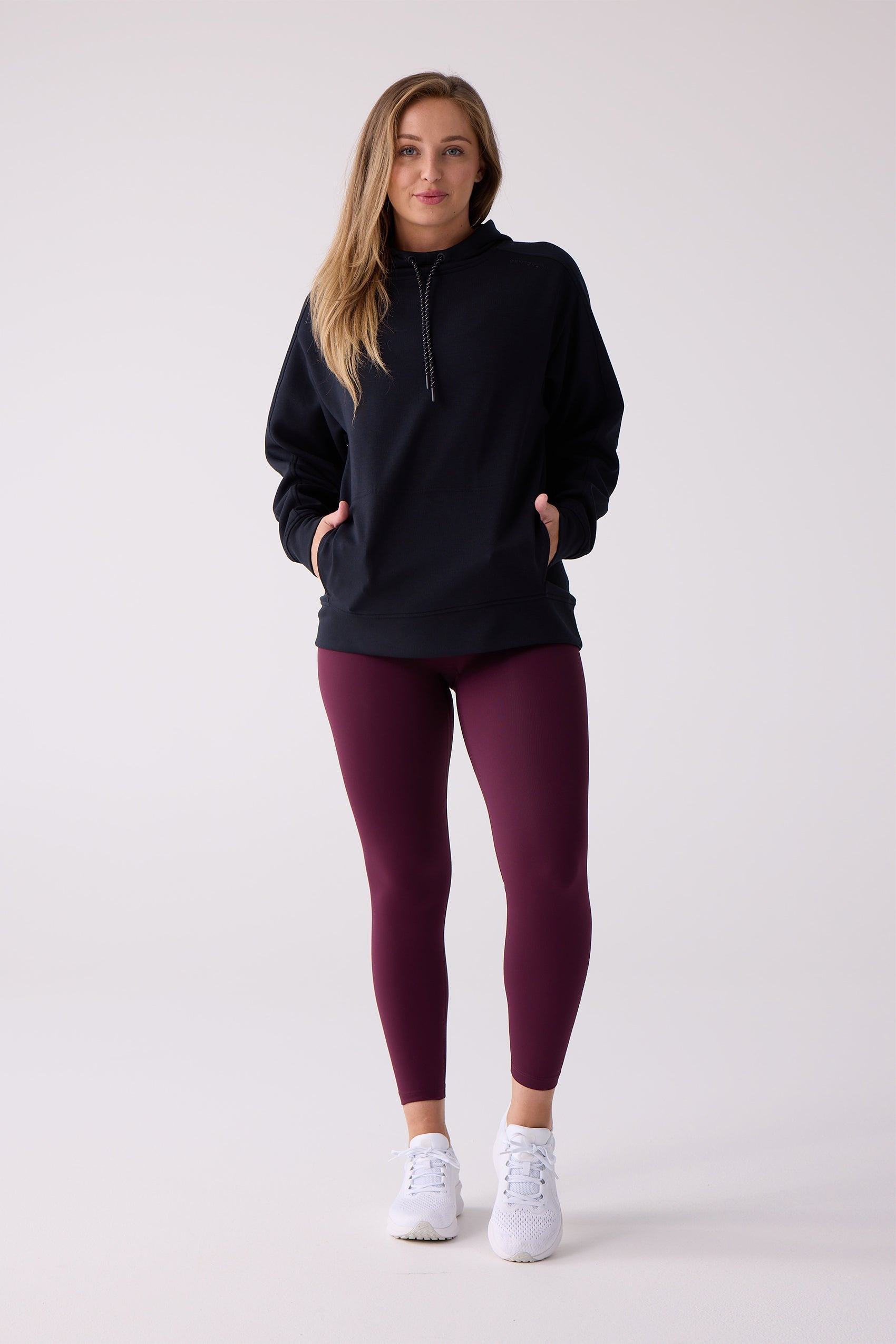 Women's dark navy hooded sweatshirt by Centerline Athletics, with drawstring hood and front pocket, styled with plum leggings and white sneakers.