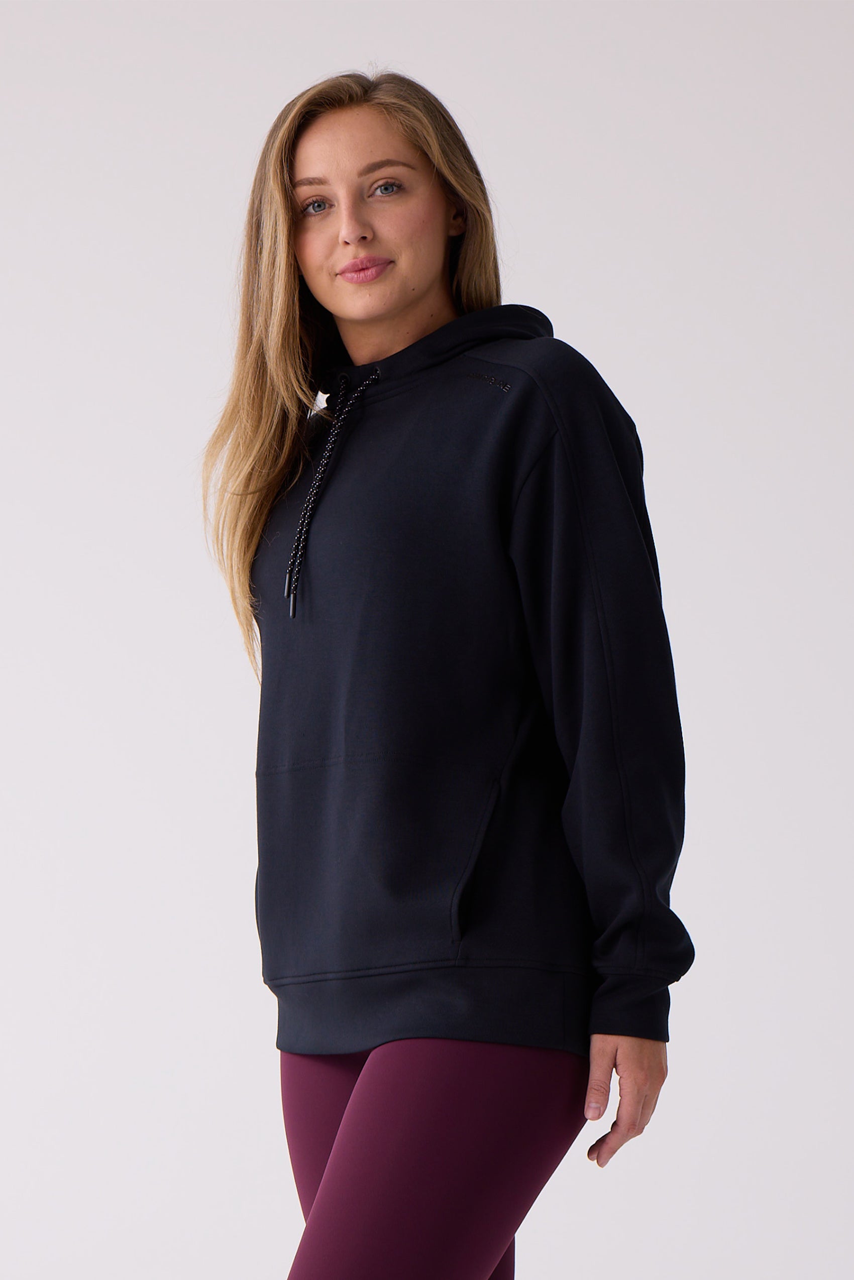 Black women's hooded sweatshirt by Centerline Athletics, with a speckled drawstring, embossed shoulder logo, and worn with maroon leggings.
