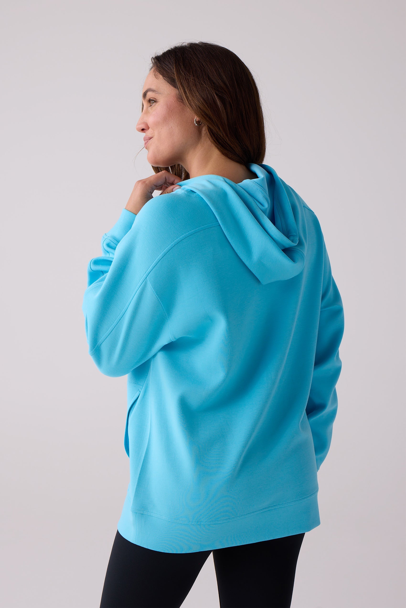 Bright turquoise hooded sweatshirt by Centerline Athletics, relaxed fit, side view on a woman with dark hair and black leggings.