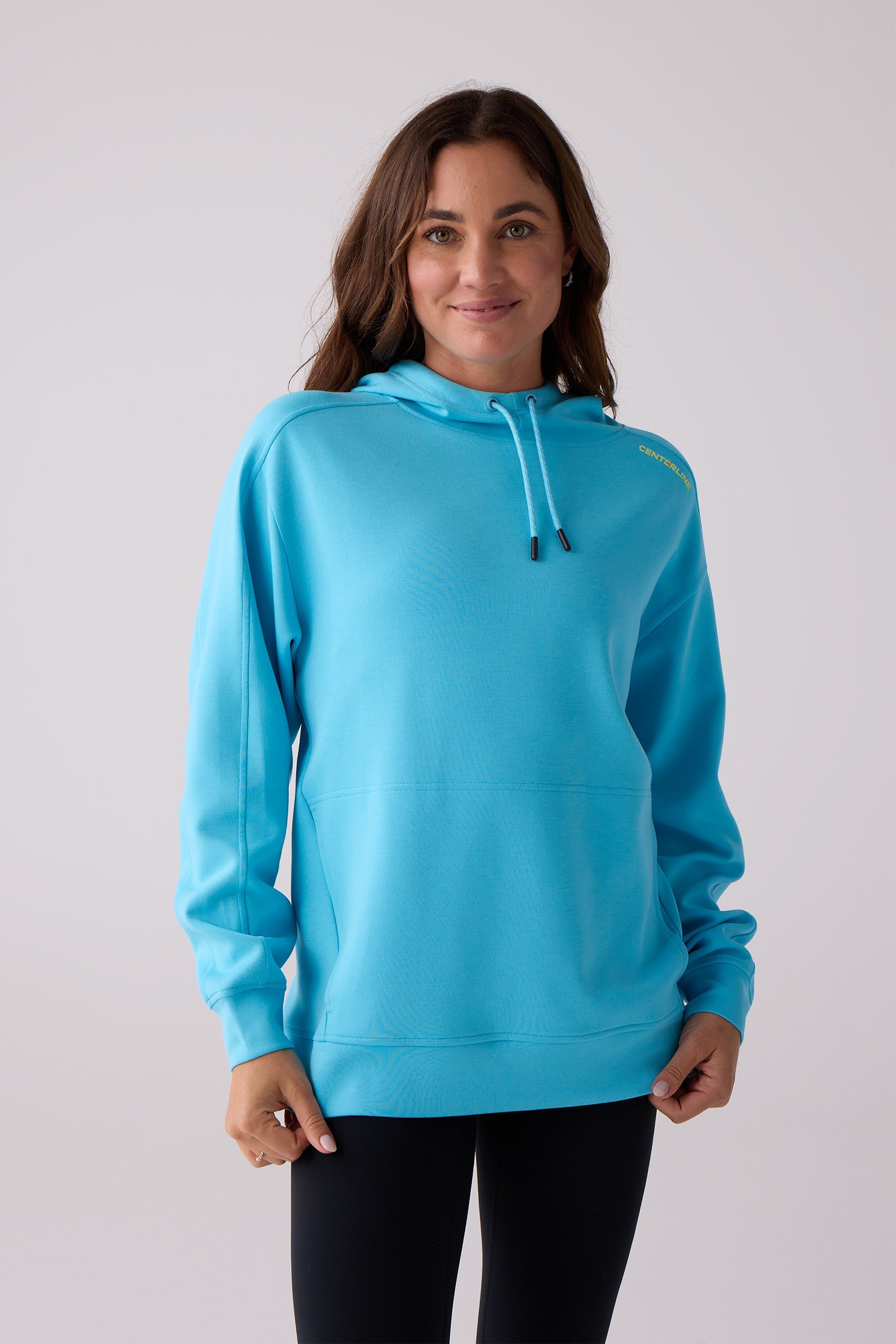 Bright blue women's hooded sweatshirt by Centerline Athletics with a drawstring hood, kangaroo pocket, and yellow "CENTERLINE" text on the shoulder, worn with black leggings.