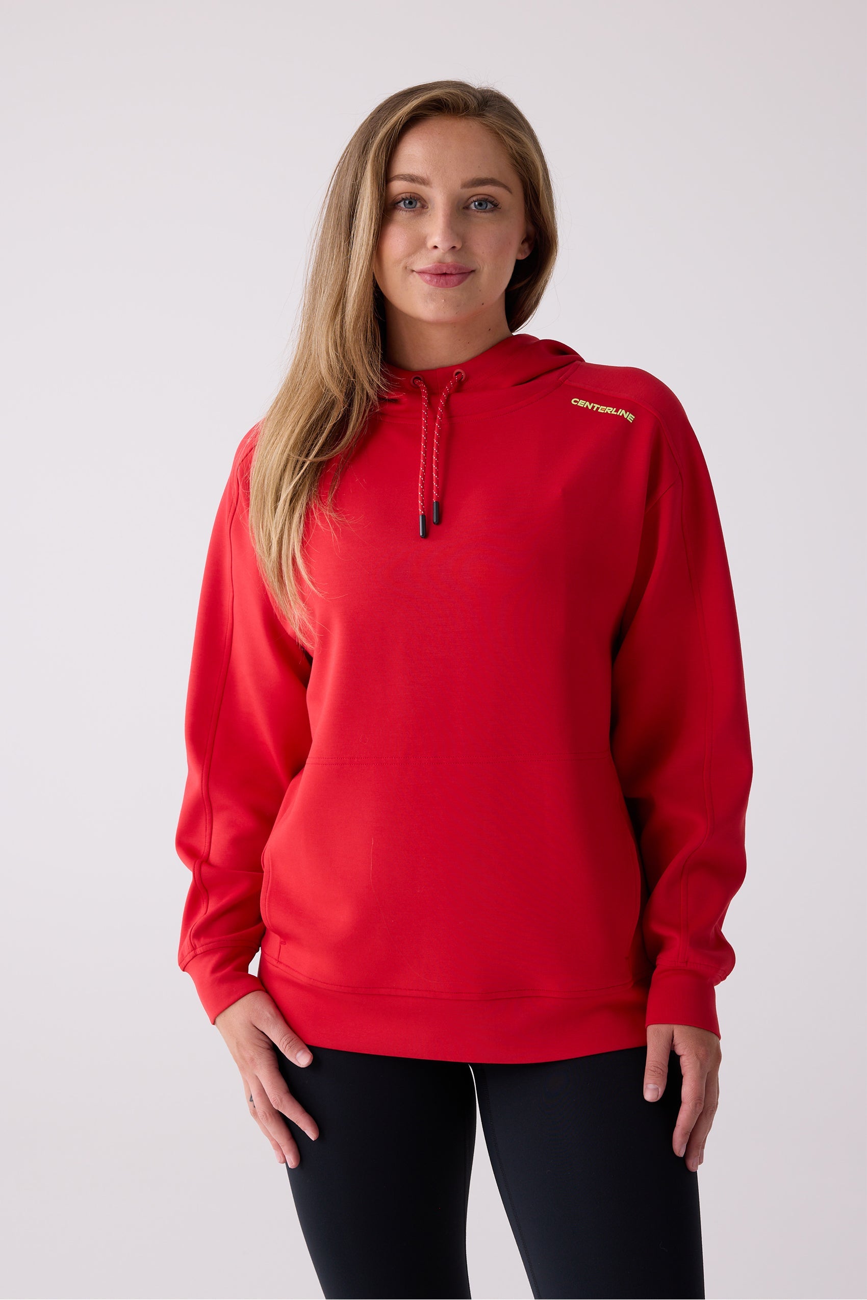 Red women's hooded sweatshirt by Centerline Athletics, with a yellow shoulder logo, drawstrings, and front pouch pocket, styled with black leggings.