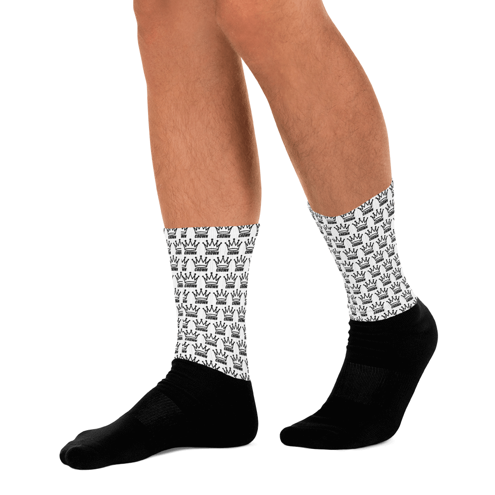 Man's legs wearing white socks with black crown pattern and black socks on feet, black background.