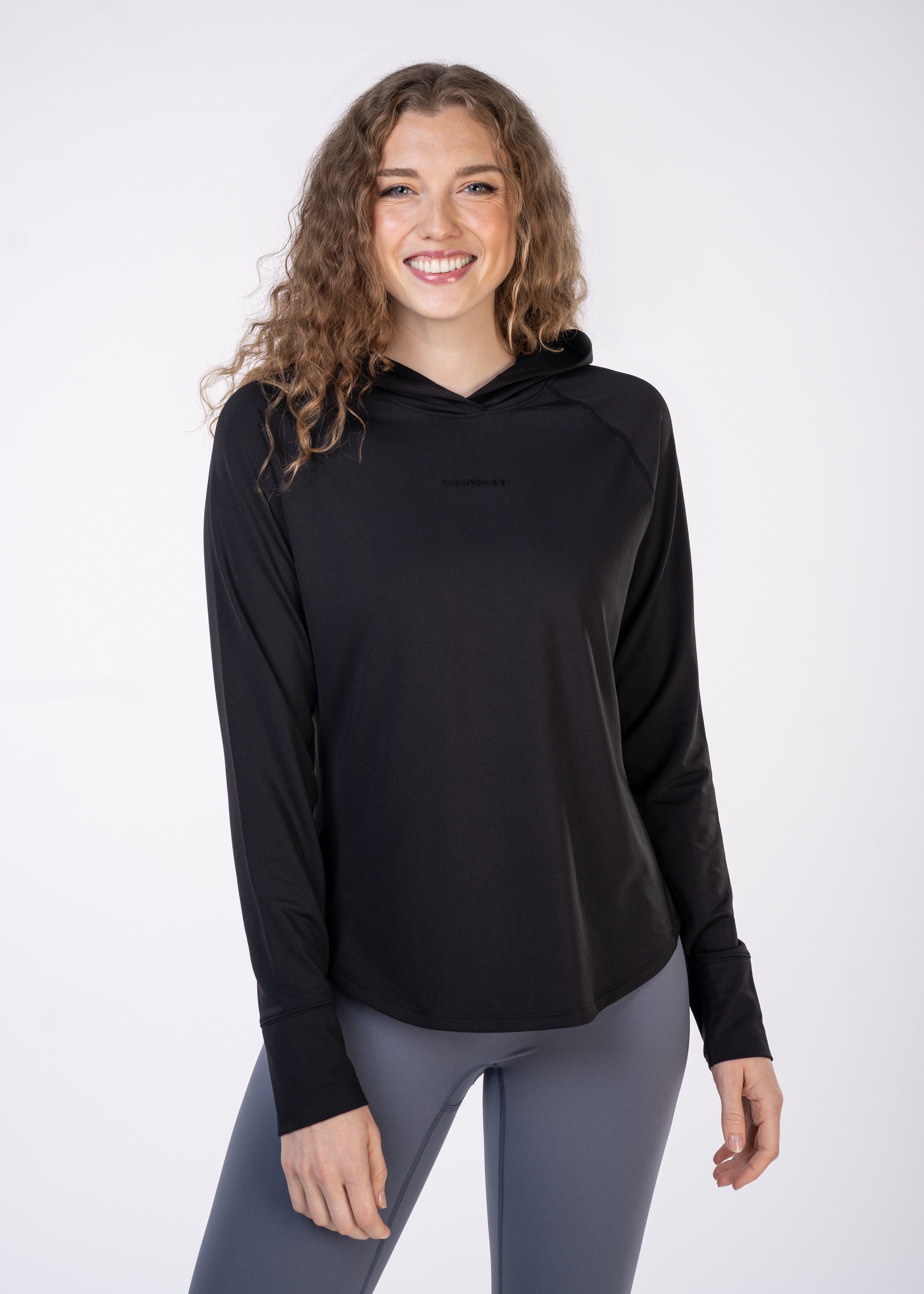Woman in black hoodie and gray leggings standing in front of white background.