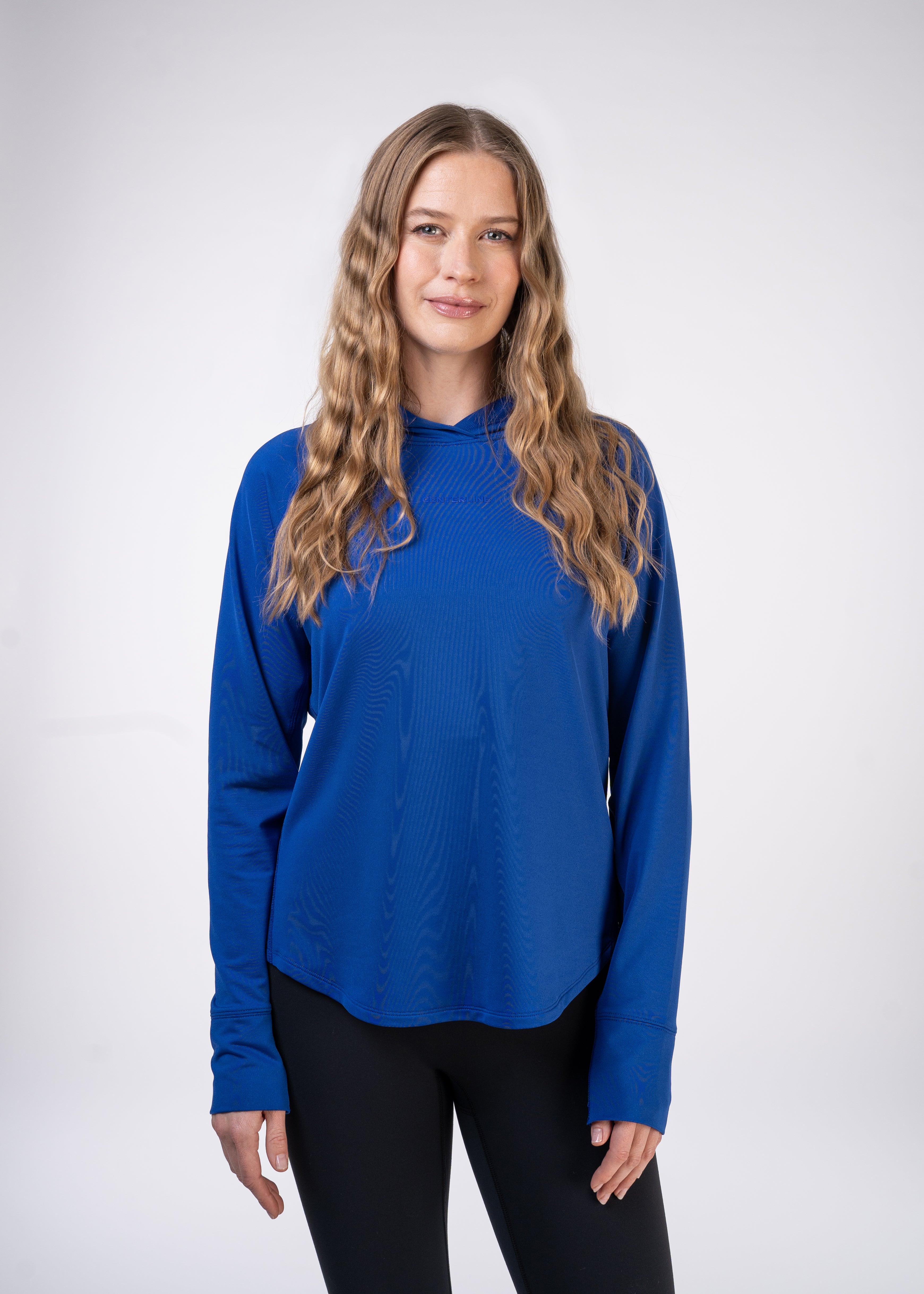 A woman in a blue hoodie and black leggings stands against a white background.