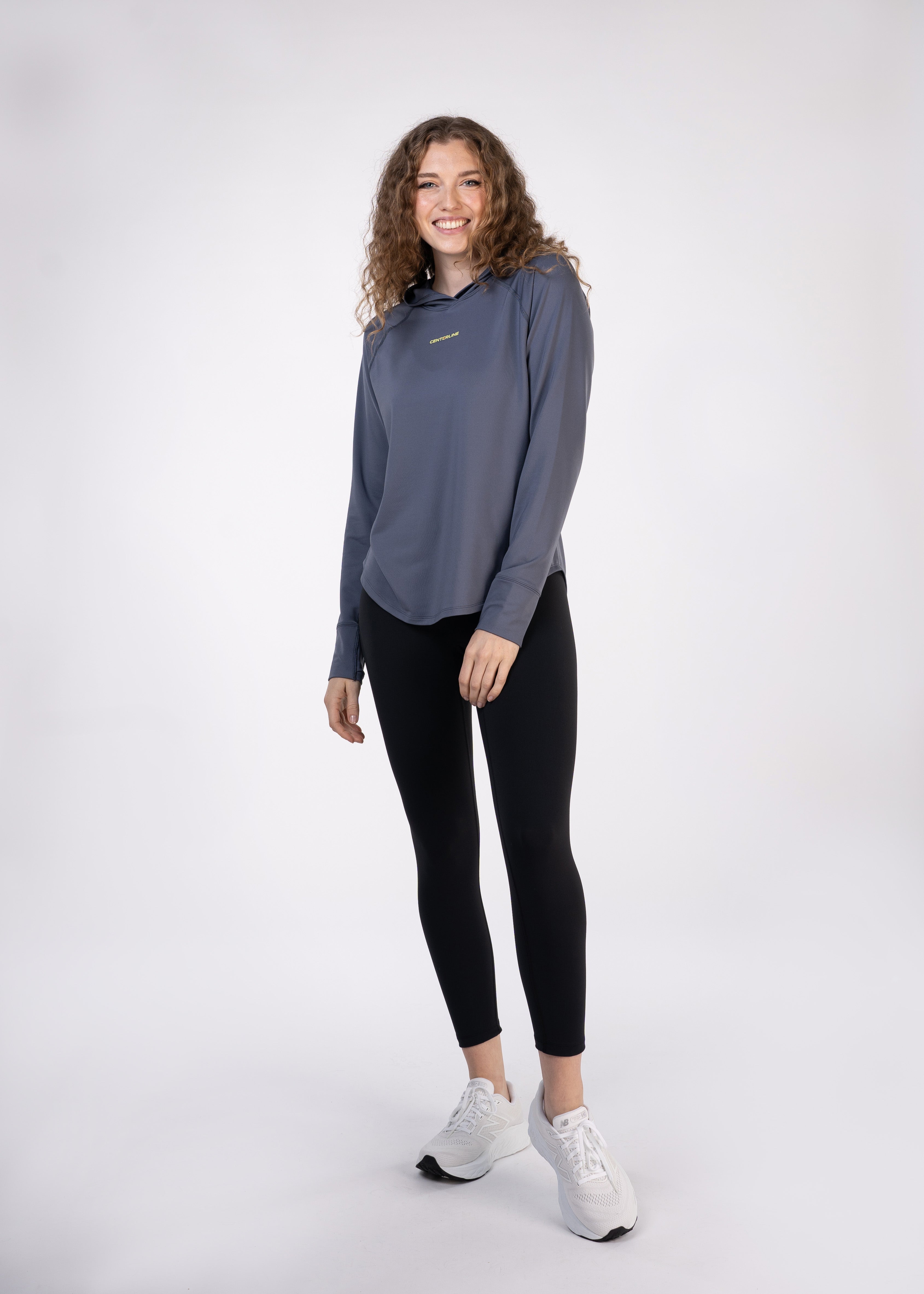 Woman standing in gray hoodie and black leggings, white sneakers.