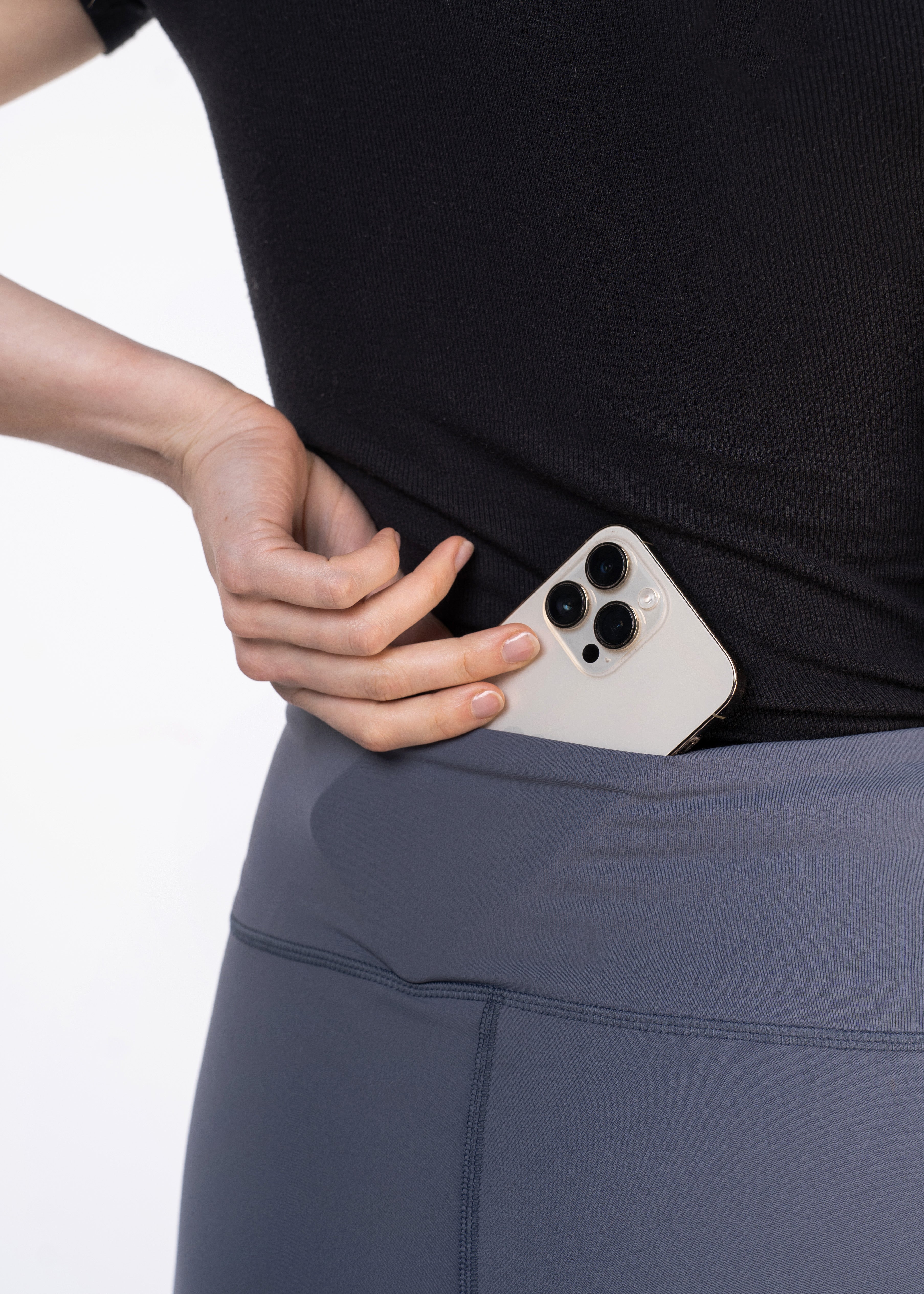 Woman putting an iPhone in the pocket of gray athletic leggings. She is wearing a black top.