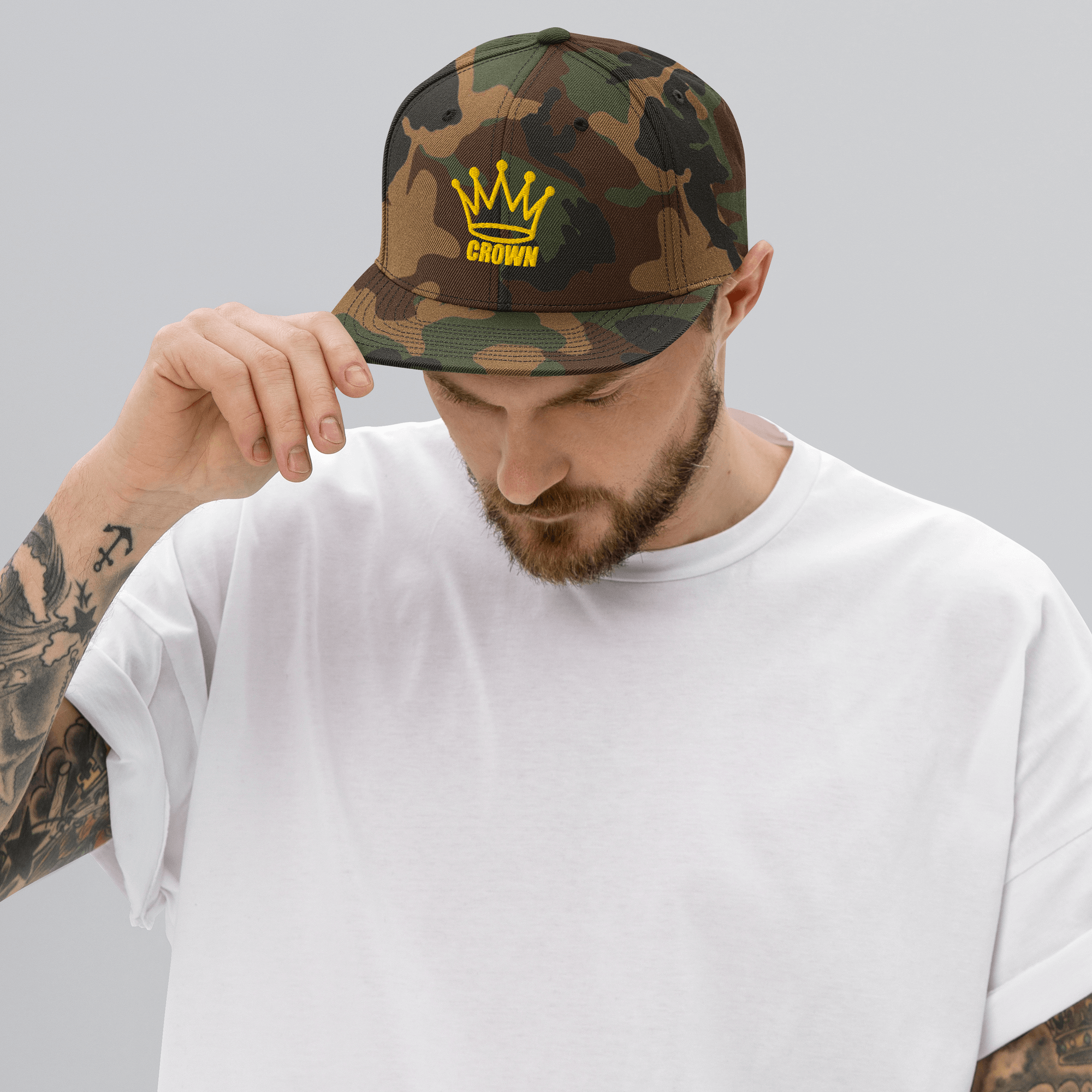 Man in a white t-shirt wearing a camouflage hat with a yellow crown logo.