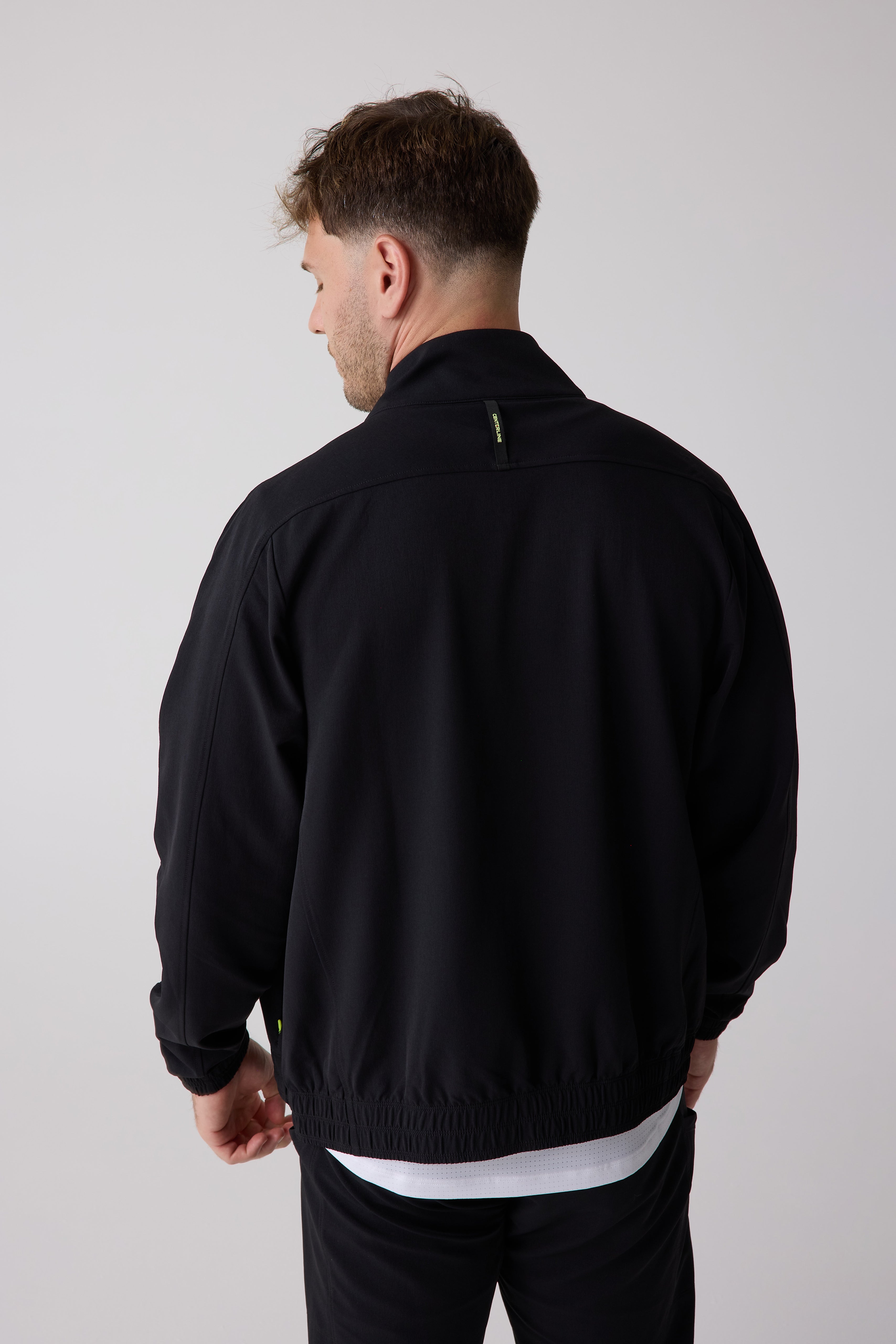 Black Men's Courtside Track Jacket by Centerline Athletics, seen from the back, with a green logo tag on the collar.