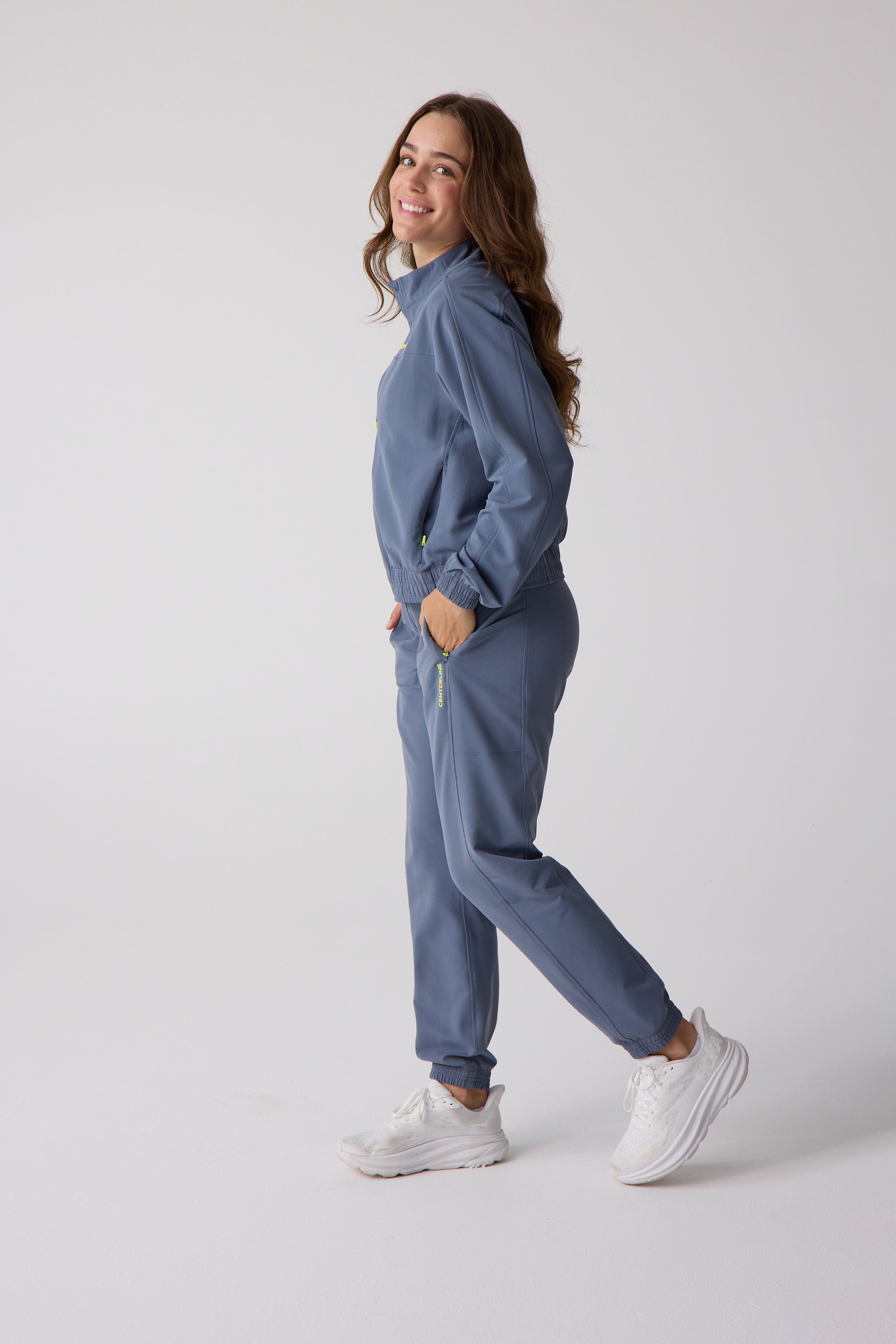 Dusty blue track pants by Centerline Athletics with neon yellow 'CENTERLINE' text, worn with a matching track jacket.