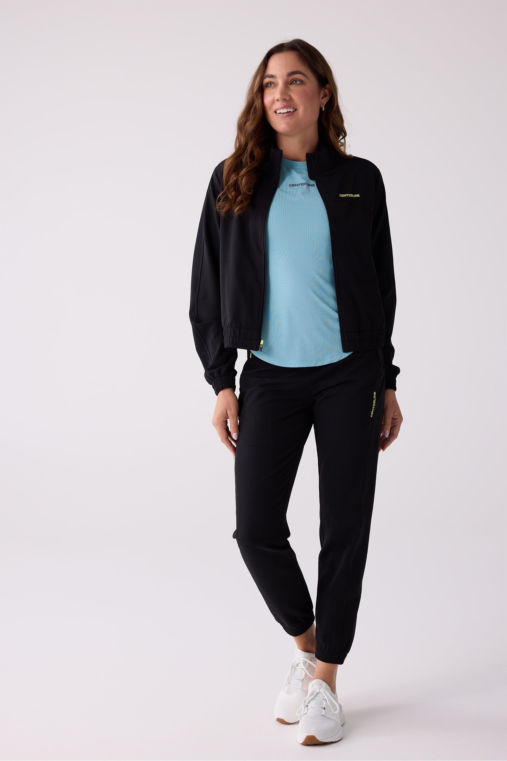Black women's Courtside track pants by Centerline Athletics, with elastic cuffs and a vertical neon yellow logo, worn with a matching jacket.