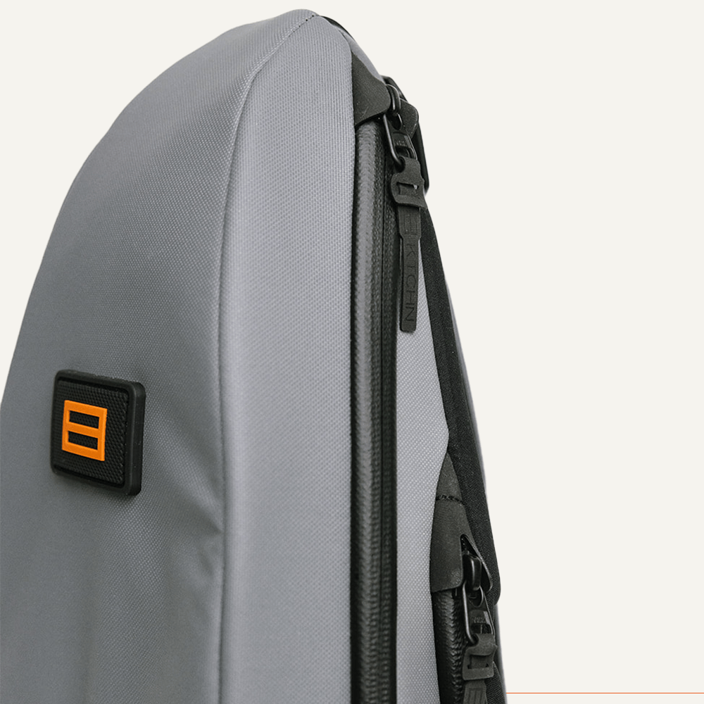 Close-up of a gray bag with black zippers and an orange logo.
