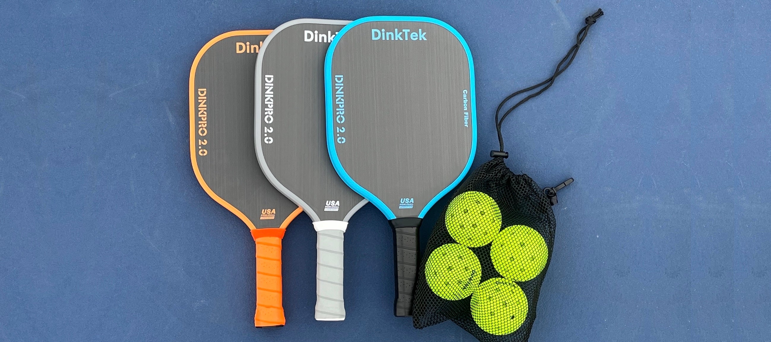 Three pickleball paddles with orange, gray, and blue handles on a blue background, accompanied by three green pickleballs in a black drawstring bag.