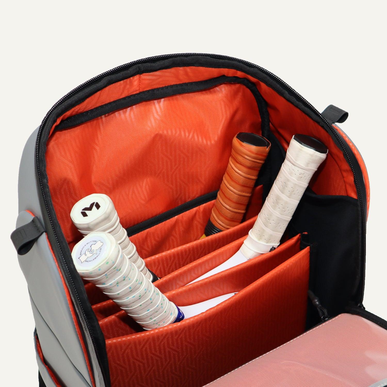 Open grey and orange pickleball bag by FORWRD, featuring an organized interior with patterned orange lining and four racket handles.