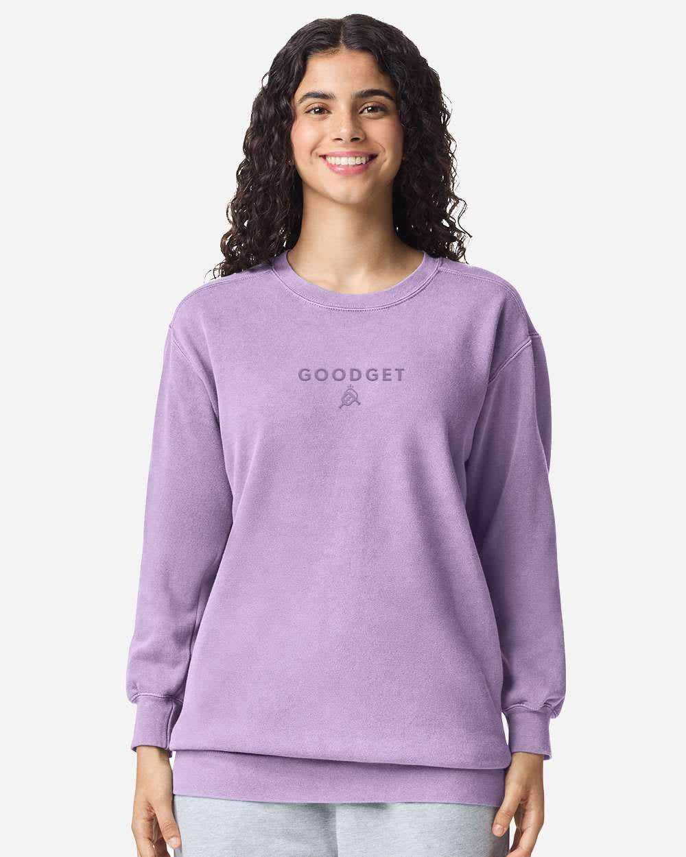 Purple crewneck sweatshirt by Good Get, featuring a subtle tone-on-tone logo, worn by a smiling woman.
