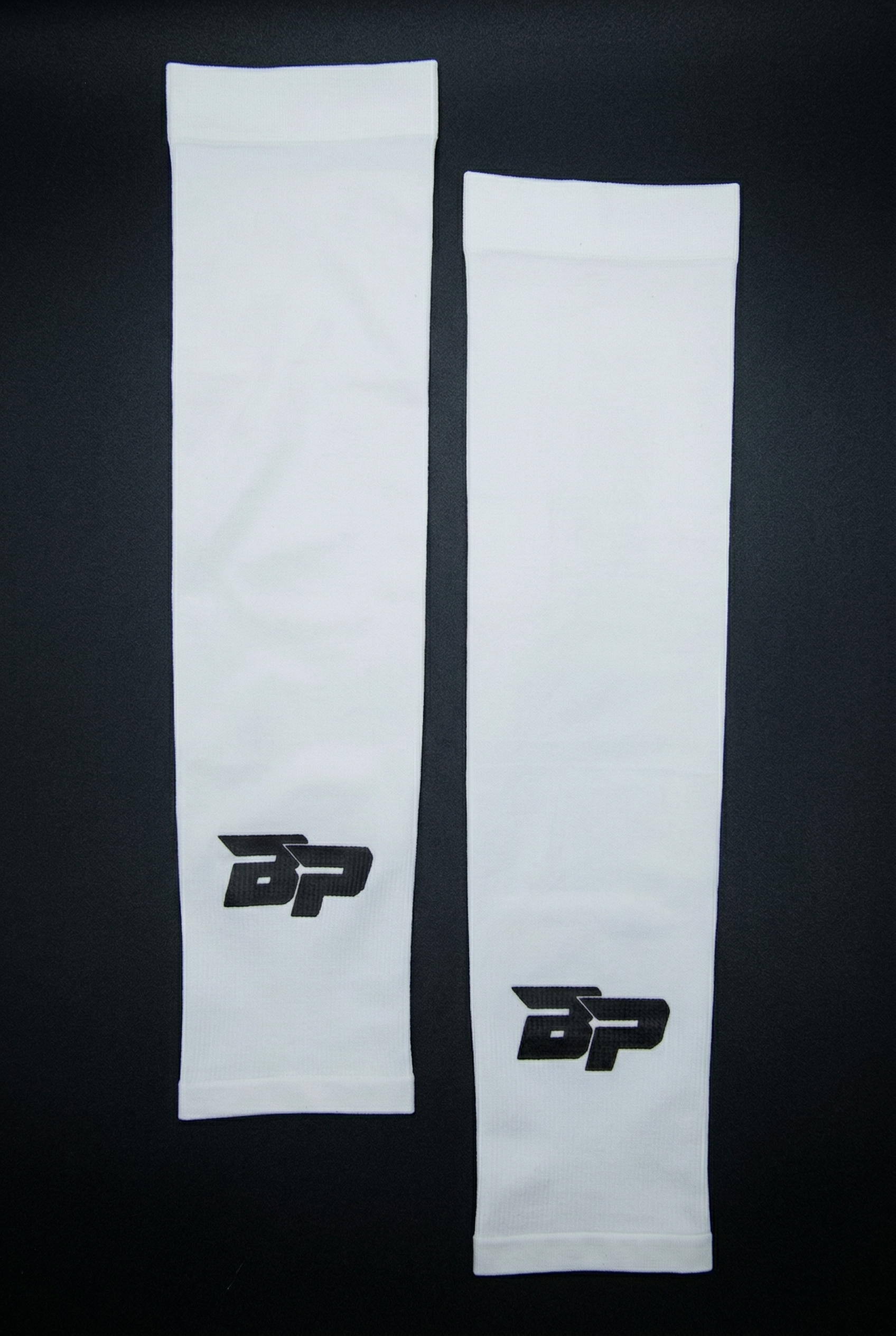 White Performance Arm Sleeves by Bodhi Pickleball, featuring a black BP logo, laid flat on a dark background.