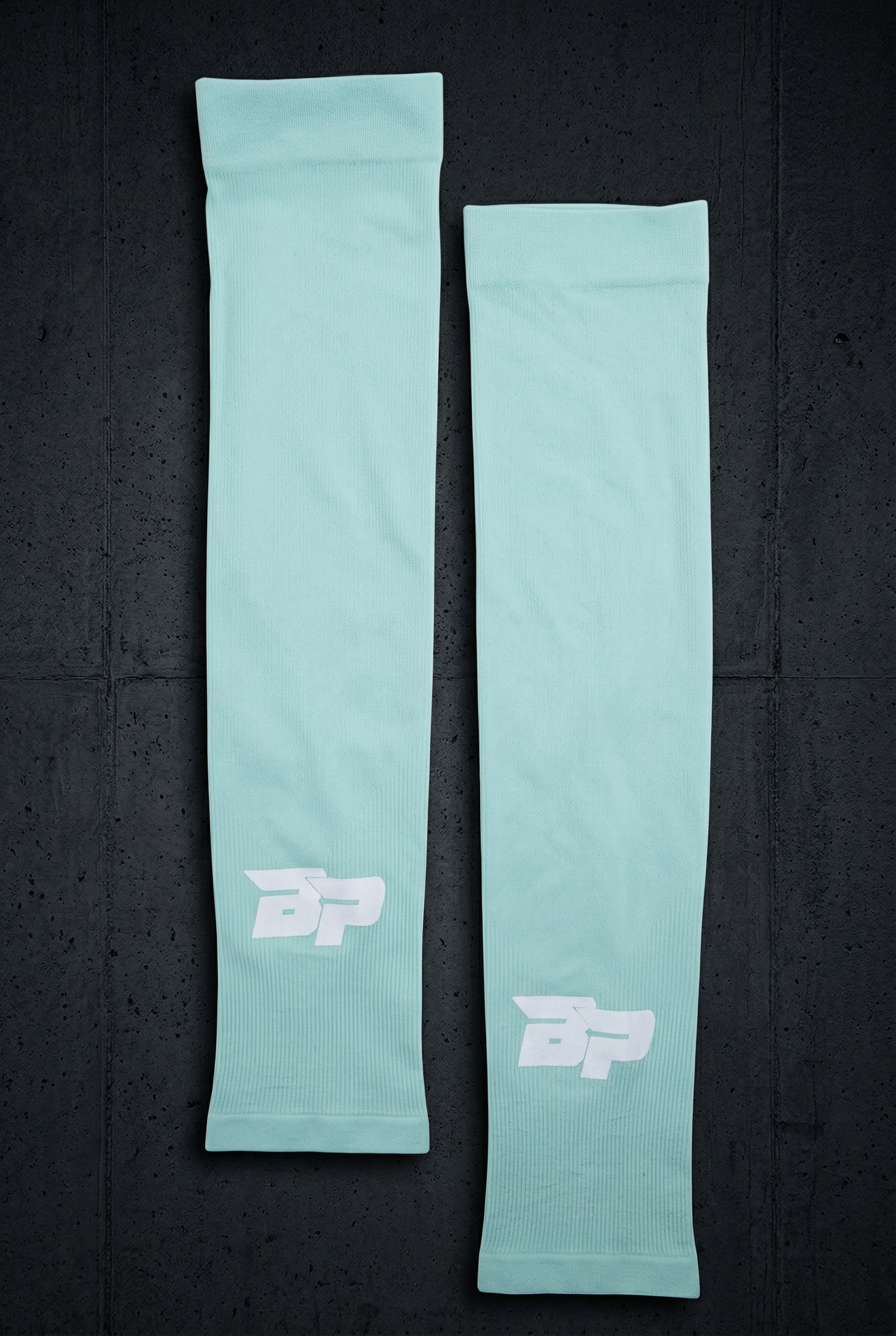 Two mint green performance arm sleeves by Bodhi Pickleball, featuring white "BP" logos and ribbed cuffs, on a dark textured background.