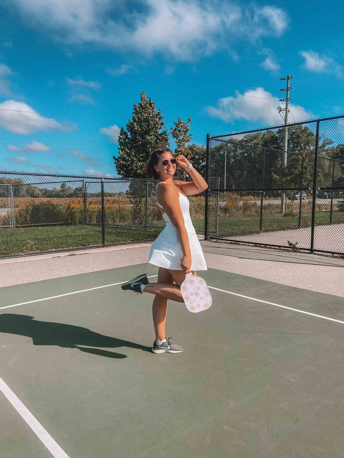 Woman in white dress holding pickleball paddle on a pickleball court.