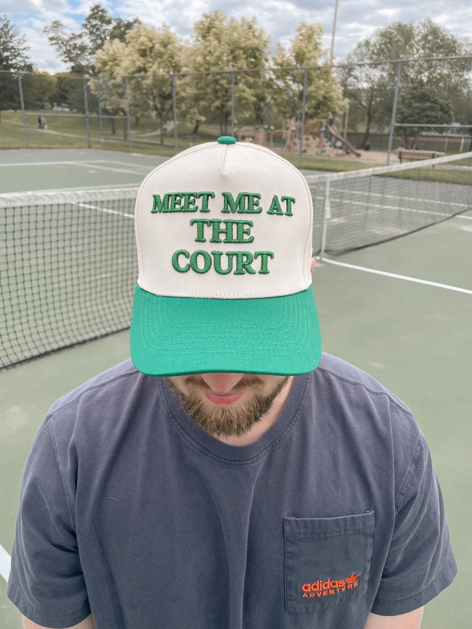 Person wearing a "Meet me at the court" hat, standing on a tennis court.