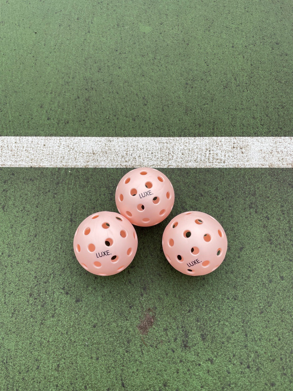 Three pink pickleballs with holes arranged on a green and white court.
