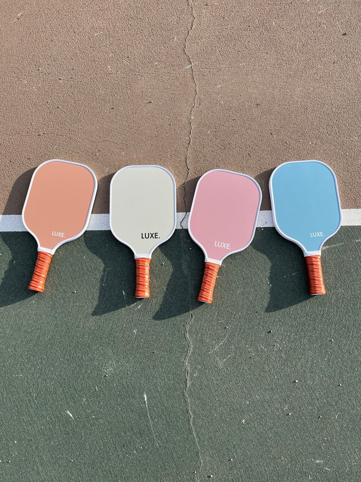 Four pickleball paddles in peach, off-white, pink, and light blue on a textured surface.