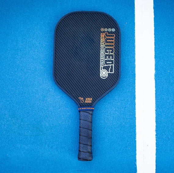 Black pickleball paddle on a blue surface with white stripe