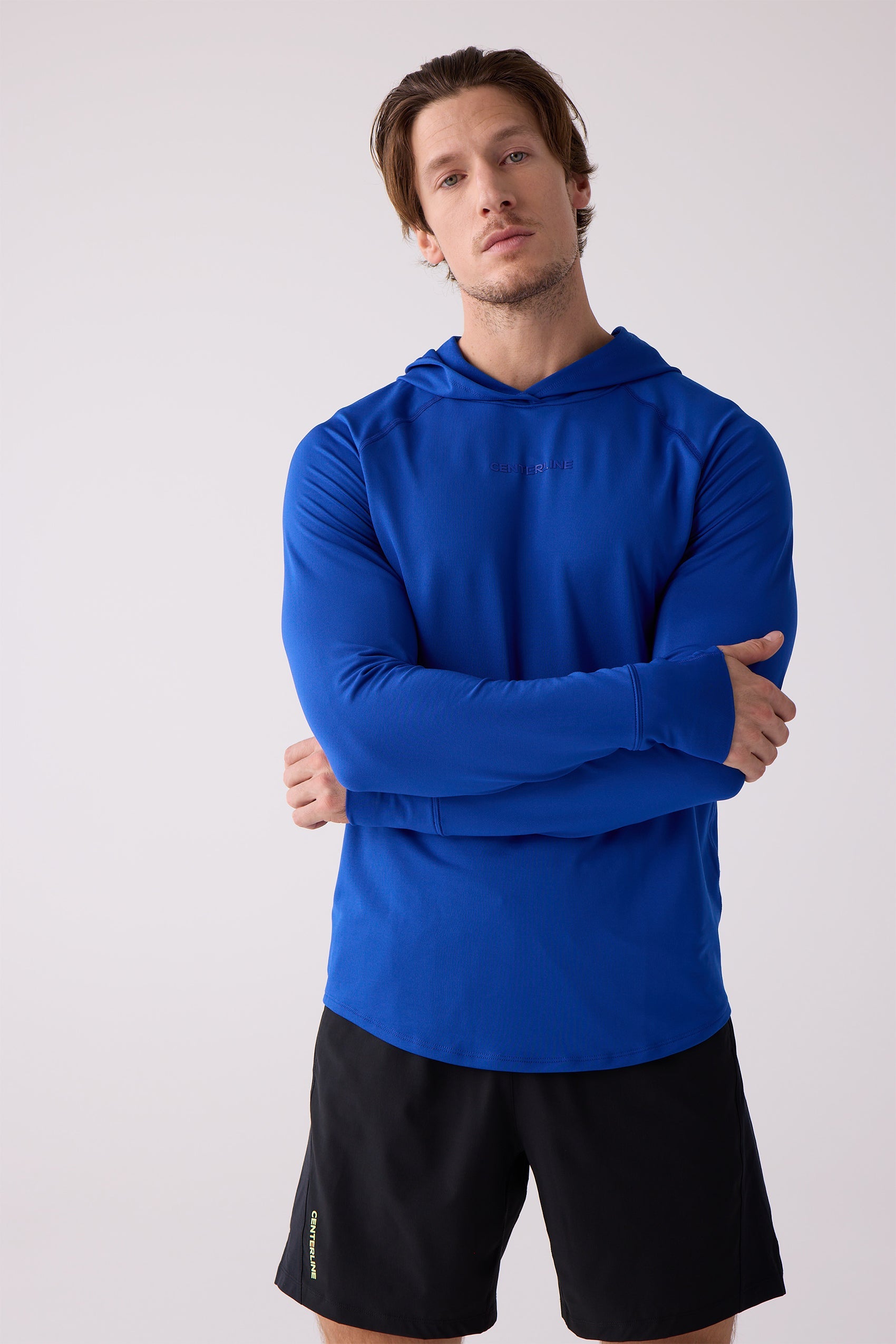 Blue men's layering hoodie by Centerline Athletics with subtle chest logo and thumbholes, worn with black shorts featuring yellow side text.