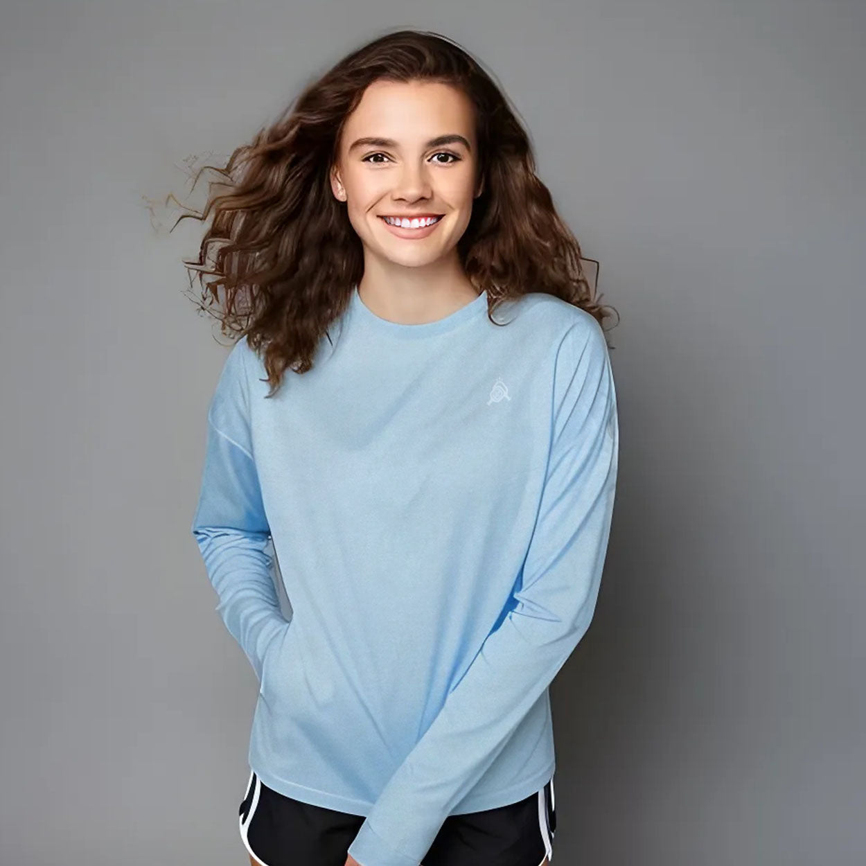 A woman in a light blue long-sleeved shirt and black shorts smiles.