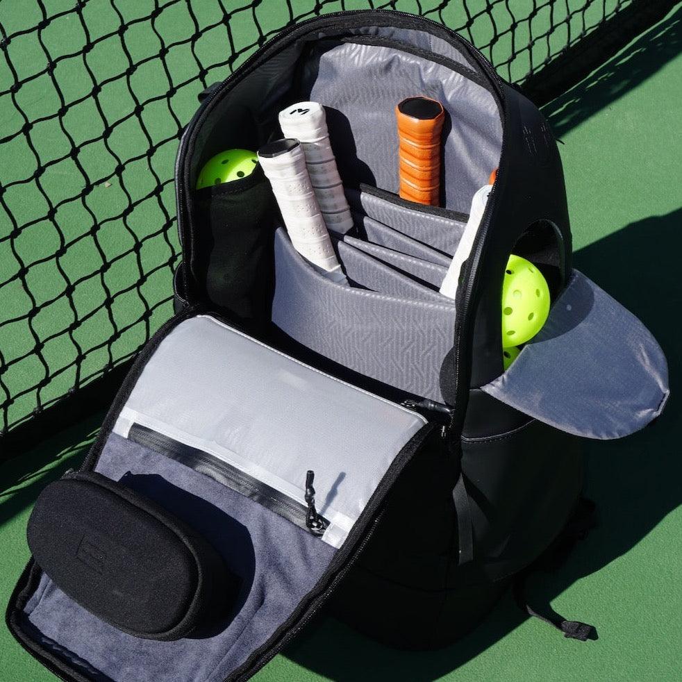 Black oval Magnetic Eyewear Case by FORWRD, open with soft lining, in a backpack on a tennis court.