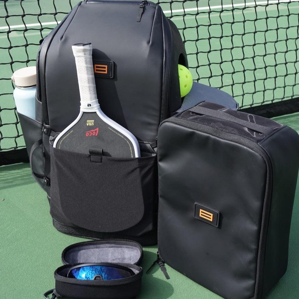 Black magnetic eyewear case by FORWRD, open with blue mirrored sunglasses on a pickleball court.