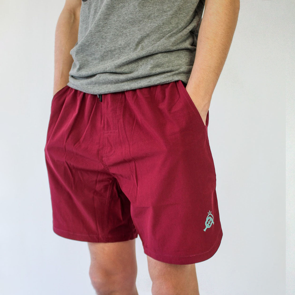 Maroon athletic shorts with a light green logo, worn with a gray t-shirt against a white background.