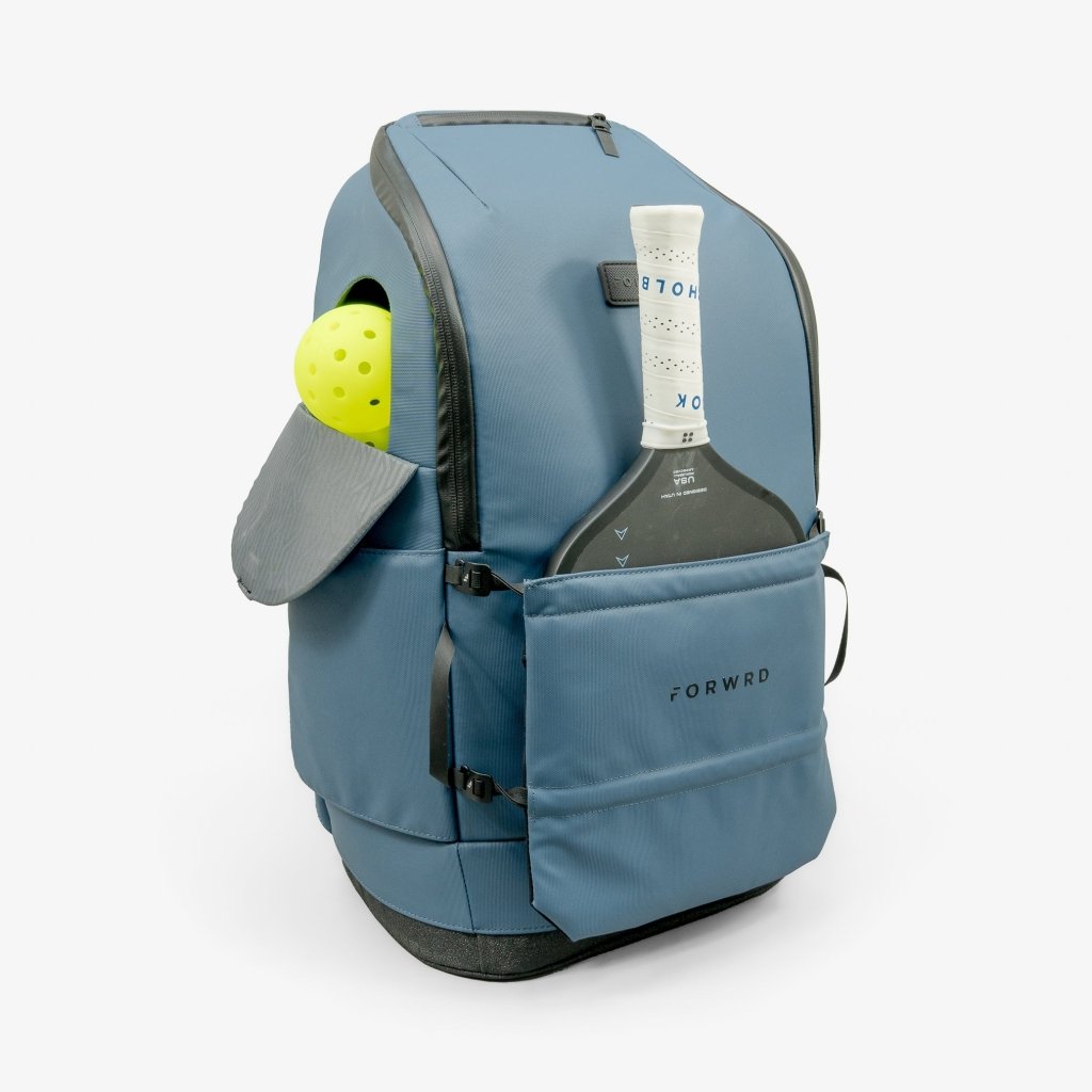 A blue pickleball backpack by FORWRD, shown from the side with a yellow pickleball and black paddle in exterior pockets.