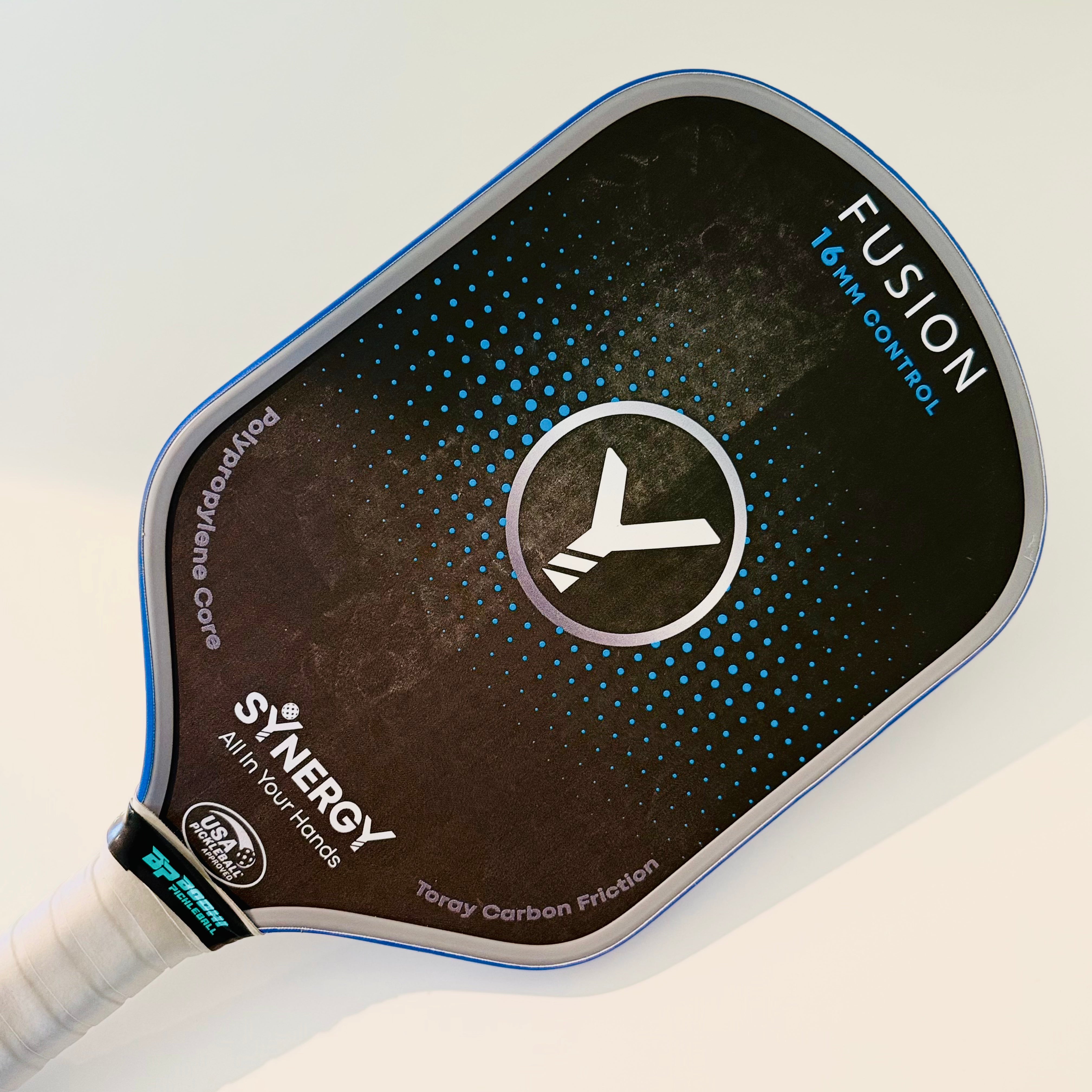 Pickleball paddle cleaner by Bodhi Pickleball, shown with an angled black pickleball paddle featuring blue dots and a white grip.