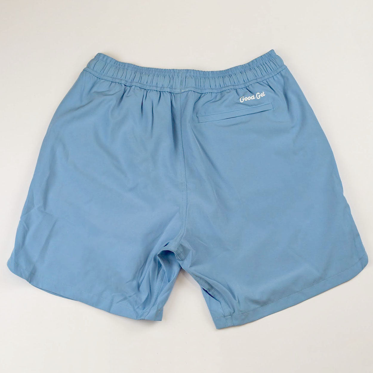 Light blue pickleball shorts by Good Get with an elastic waistband and embroidered logo above the back pocket, shown from the back.
