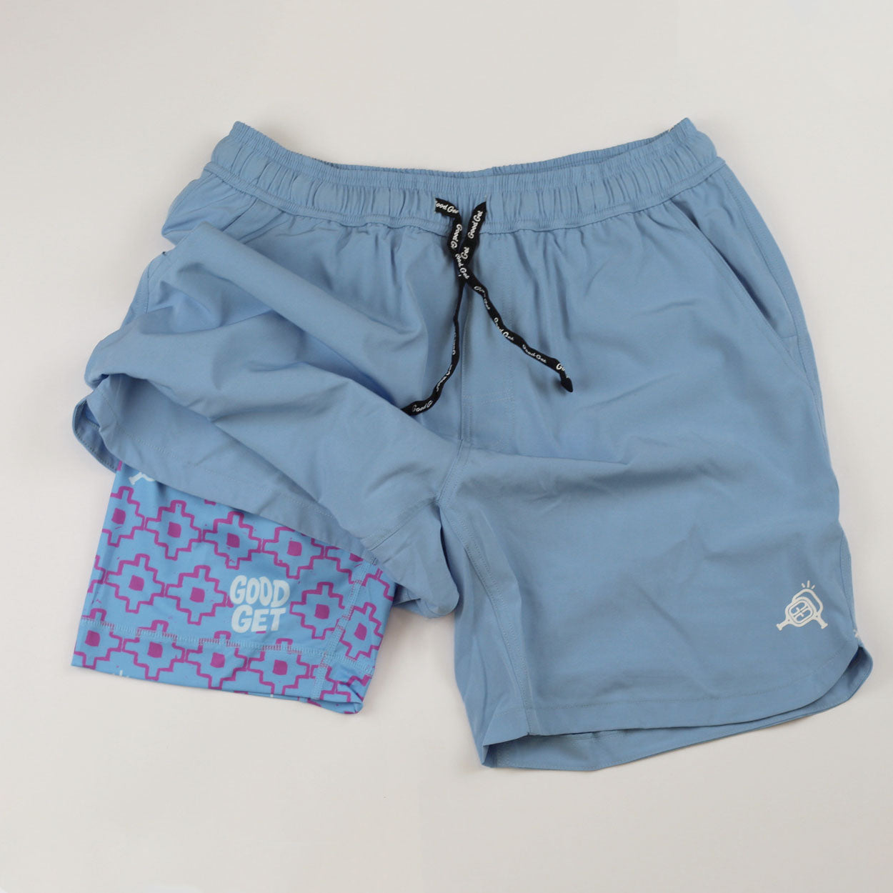 Light blue pickleball shorts by Good Get, featuring a purple geometric liner with brand text, black drawstring, and white paddle logo.