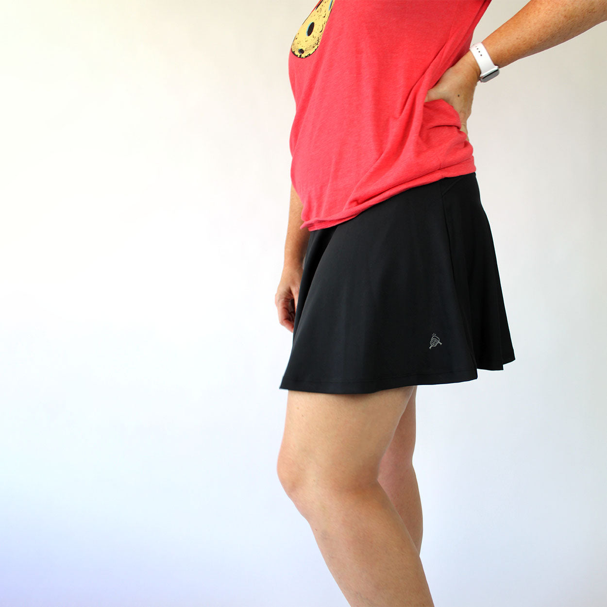 Woman in red t-shirt and black tennis skirt with logo.