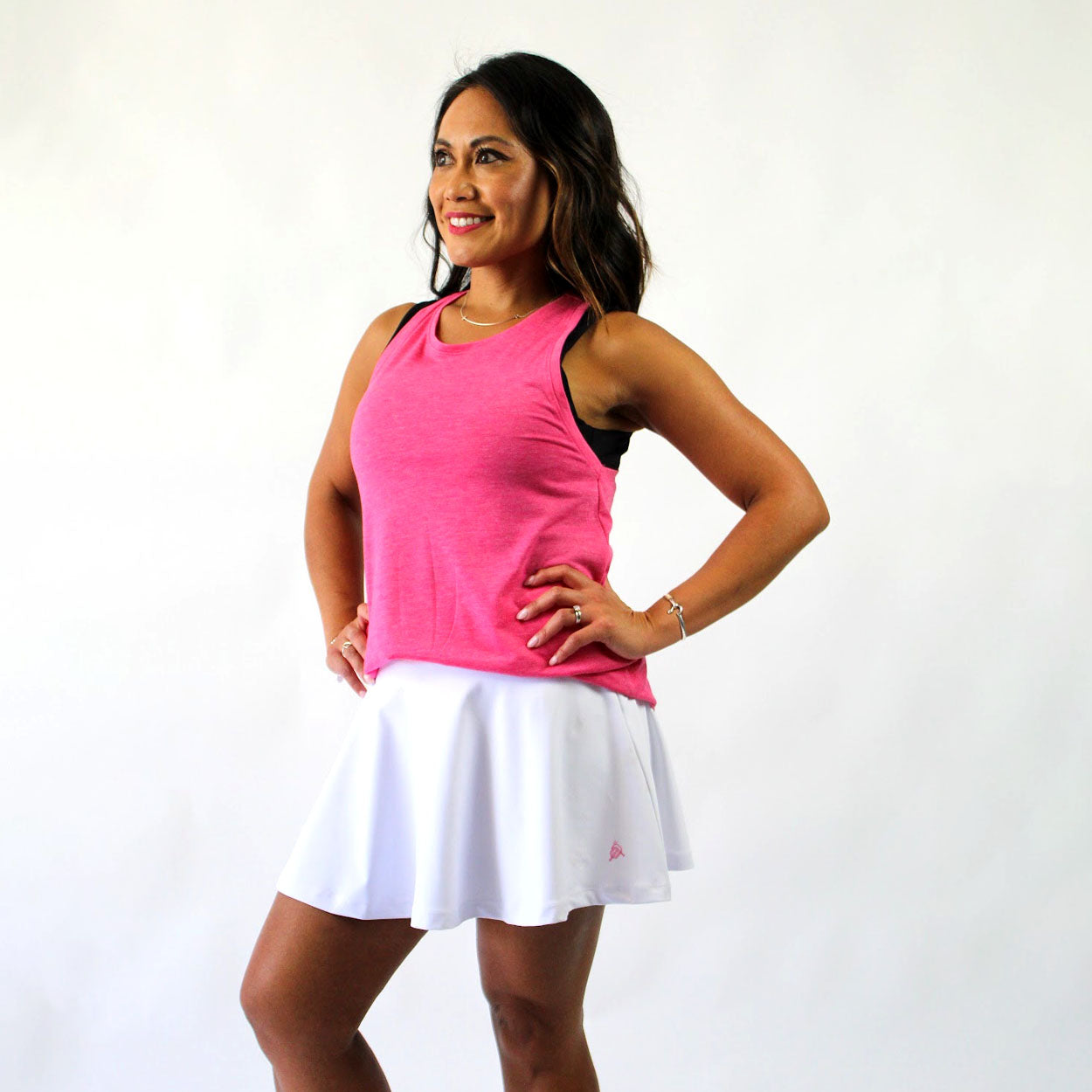 Woman in pink tank top and white tennis skirt with hands on hips.