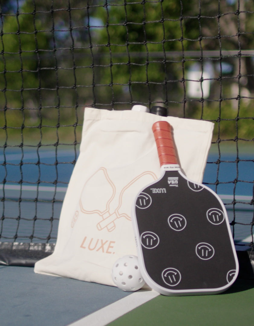 Pickleball paddle and ball, tote bag, net backdrop.