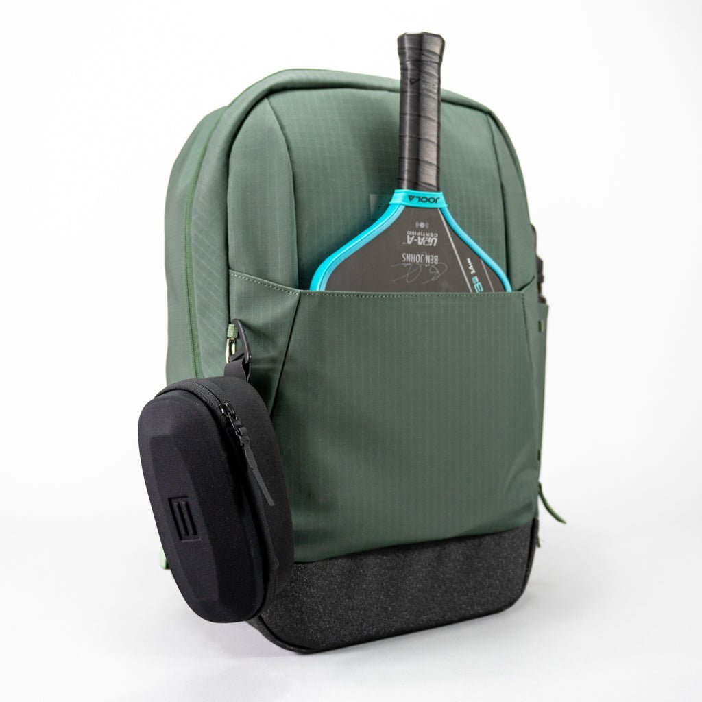 Green ribbed pickleball backpack by FORWRD features a black textured base and holds a pickleball paddle in its front pocket, with a small black case attached.